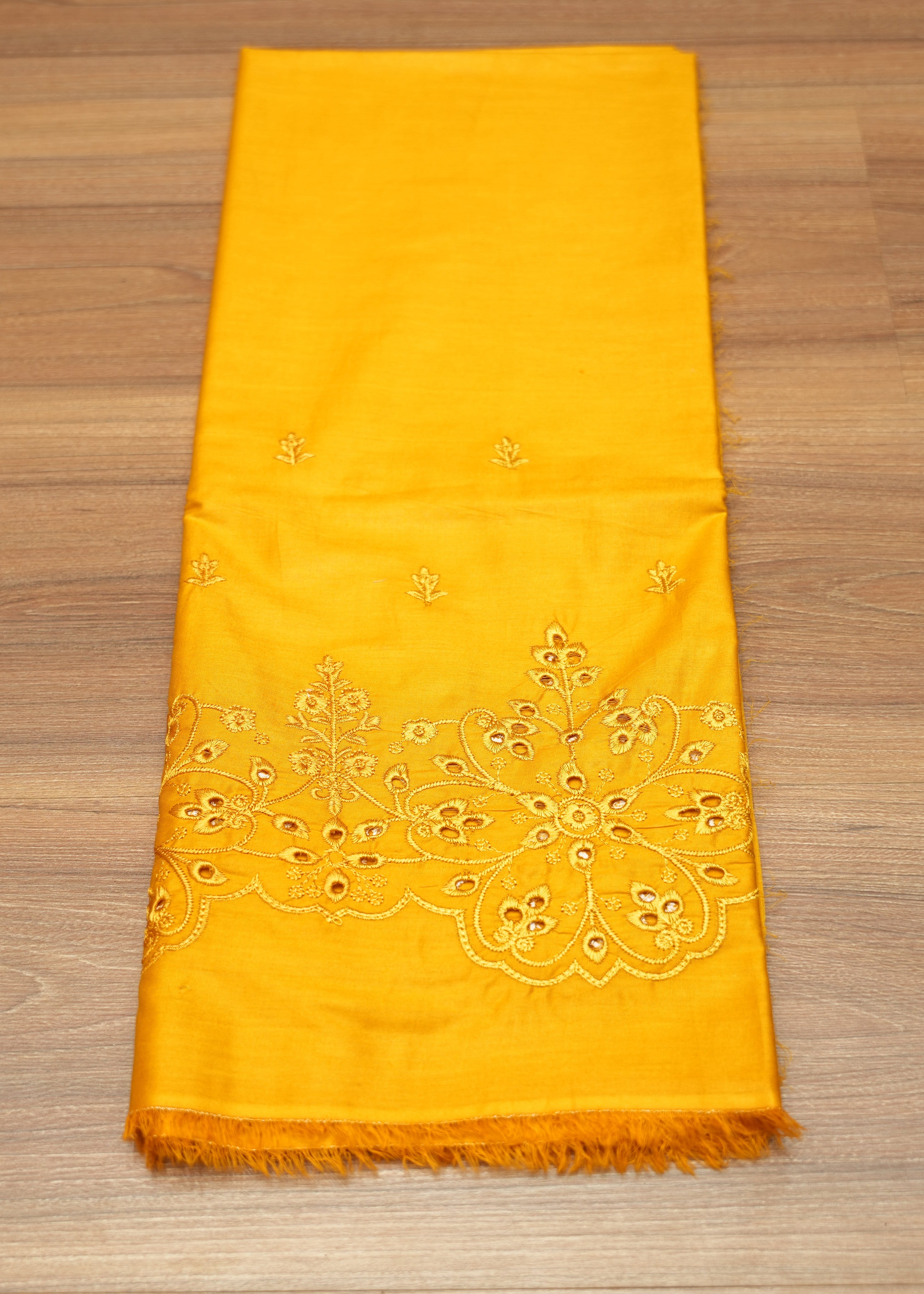 Yellow scarf with intricate white embroidery on a wooden surface