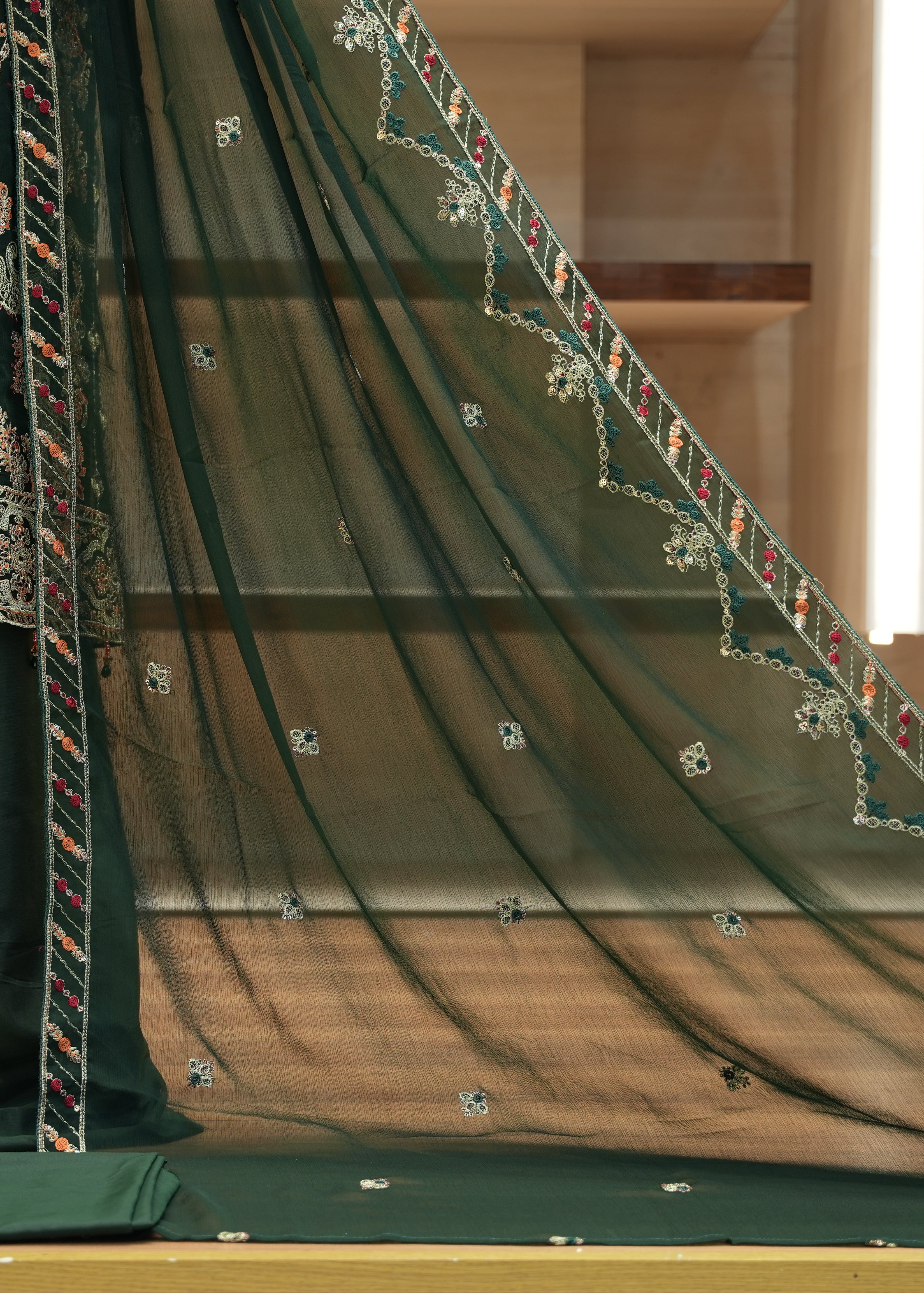 Green embroidered fabric with intricate patterns on a wooden surface.