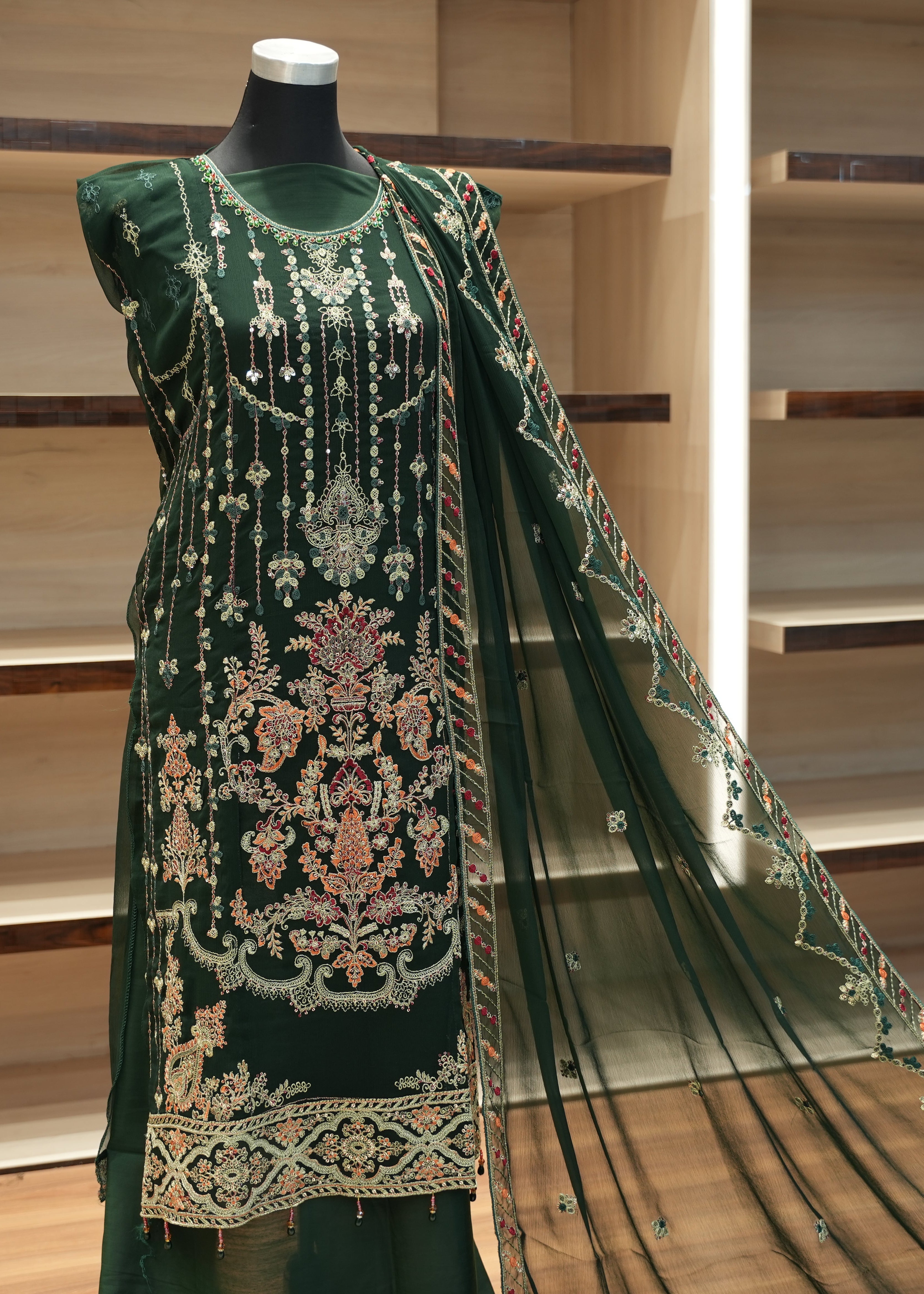 Green embroidered traditional outfit on a mannequin against a wooden shelf background