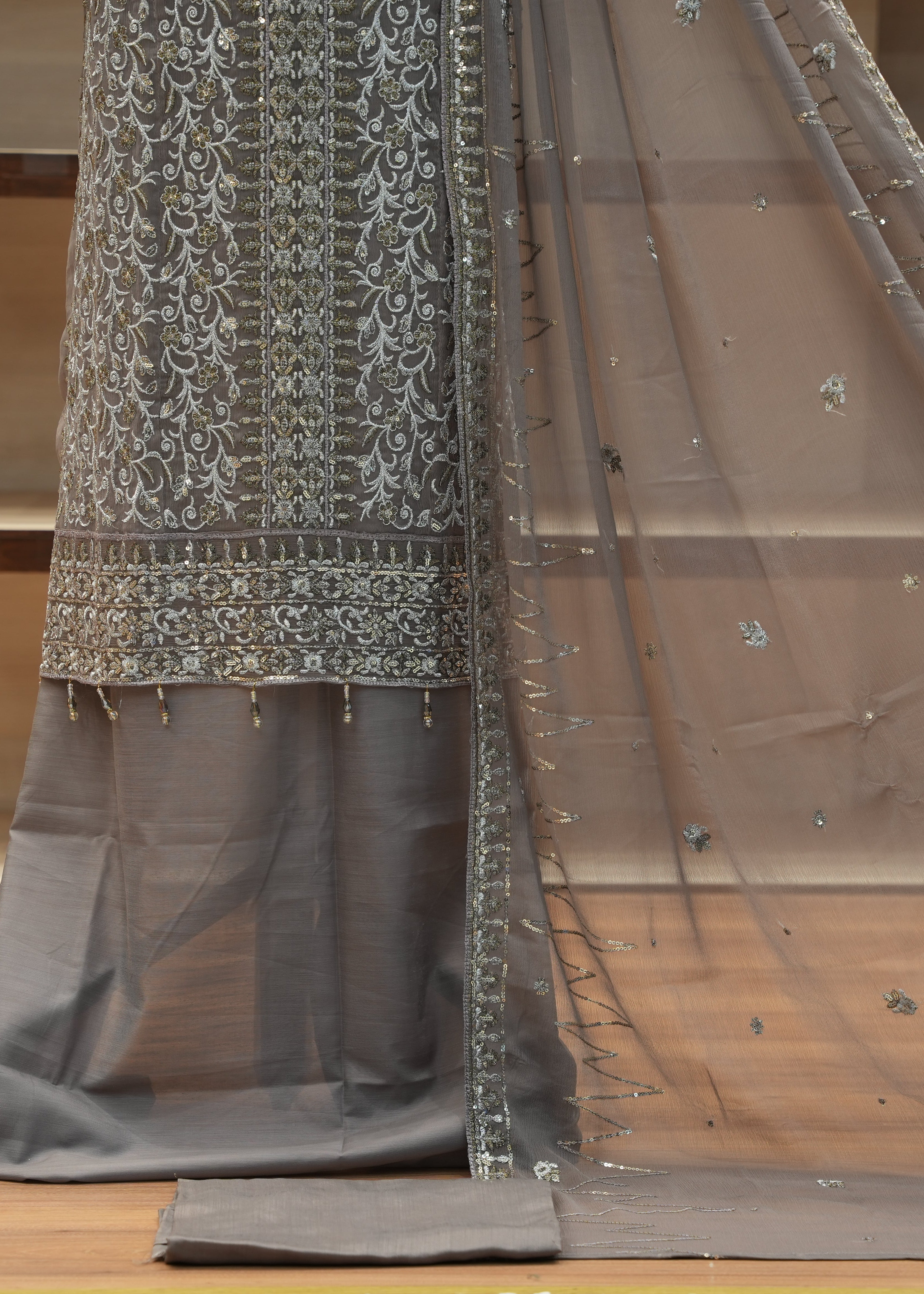 Gray traditional outfit with intricate white embroidery on a wooden floor.