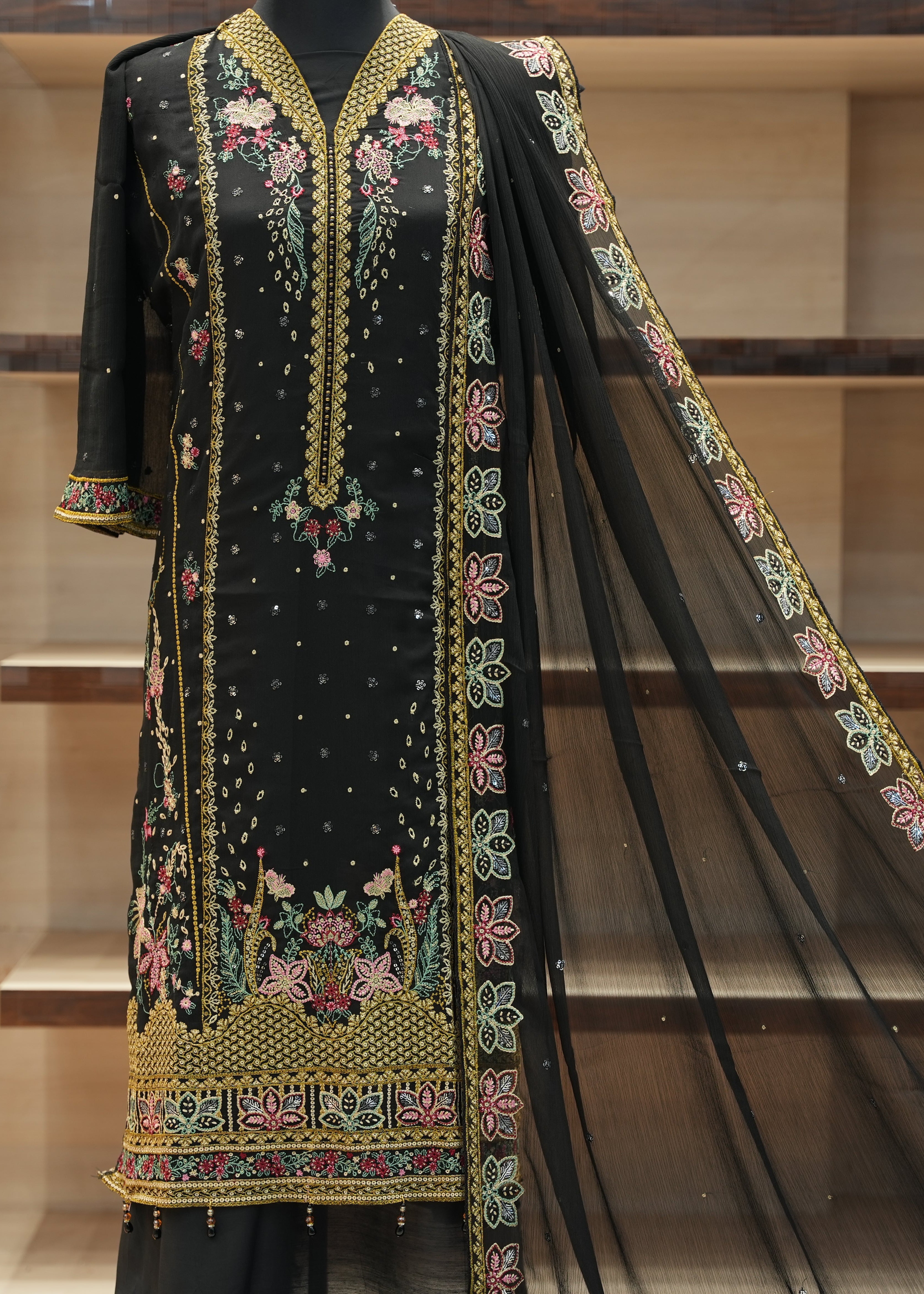 Black embroidered traditional outfit with a sheer dupatta on a wooden shelf background