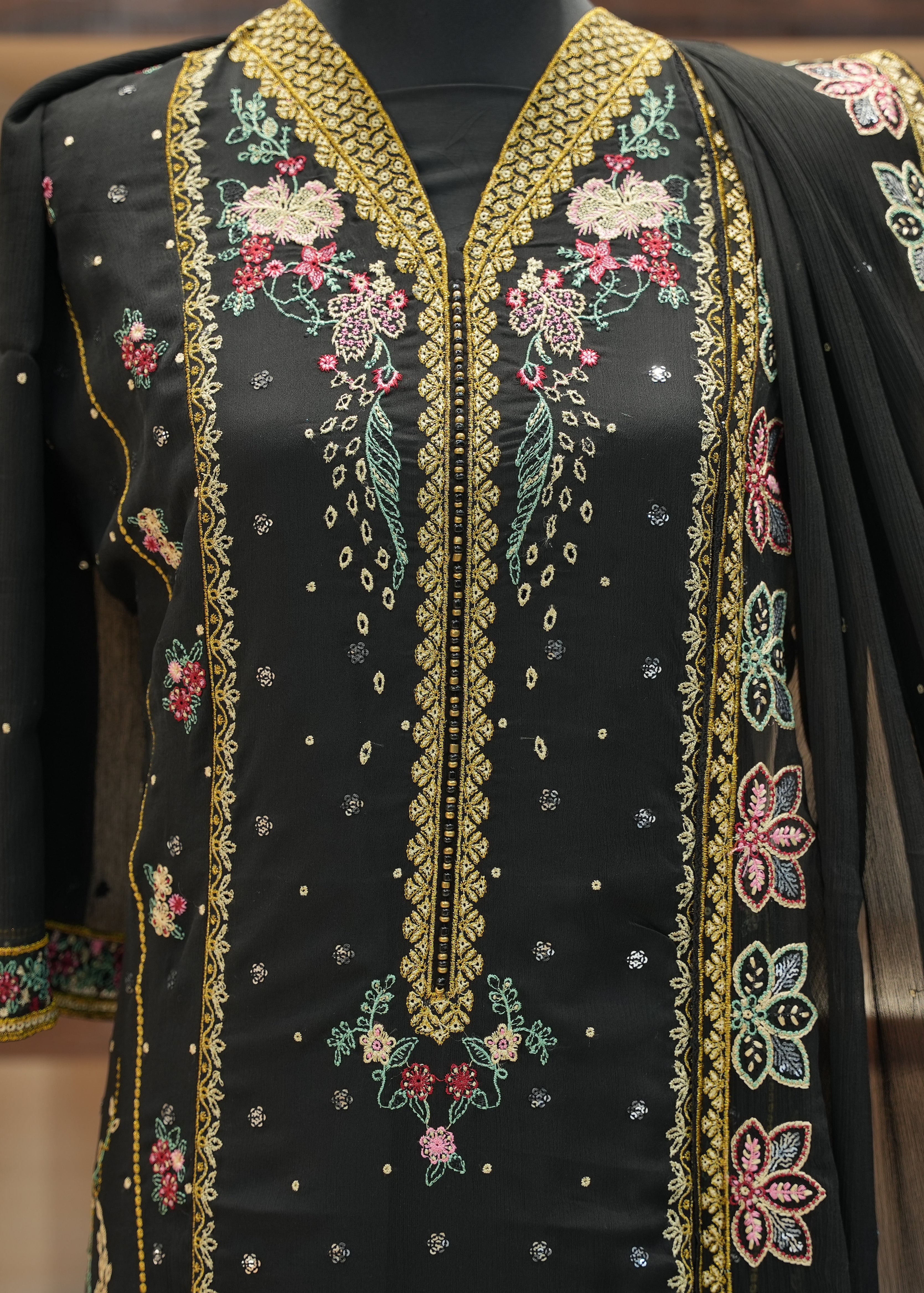 Black embroidered garment with gold and multicolor details on a mannequin.