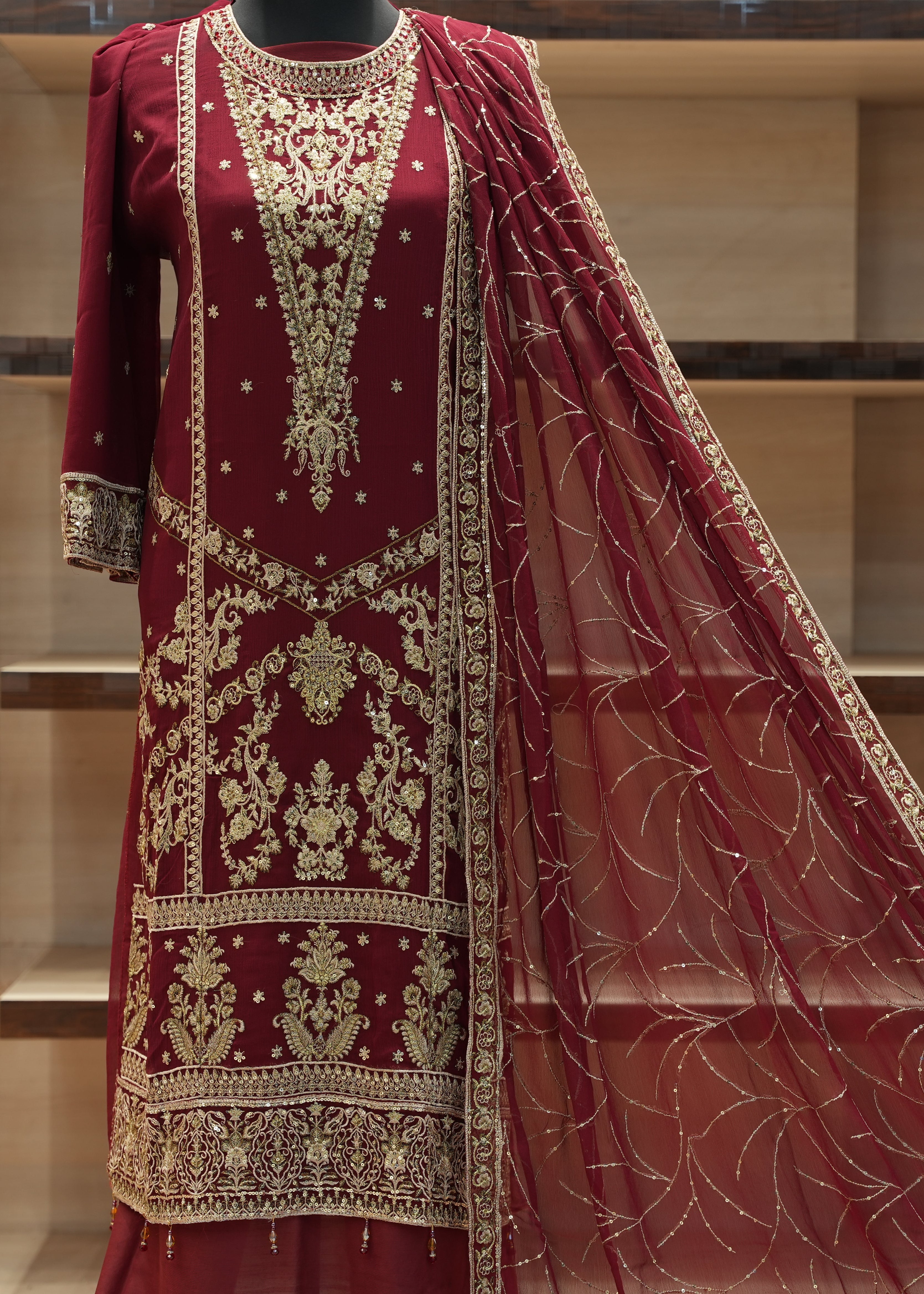 Red embroidered traditional outfit with a matching dupatta on a mannequin against a neutral background.