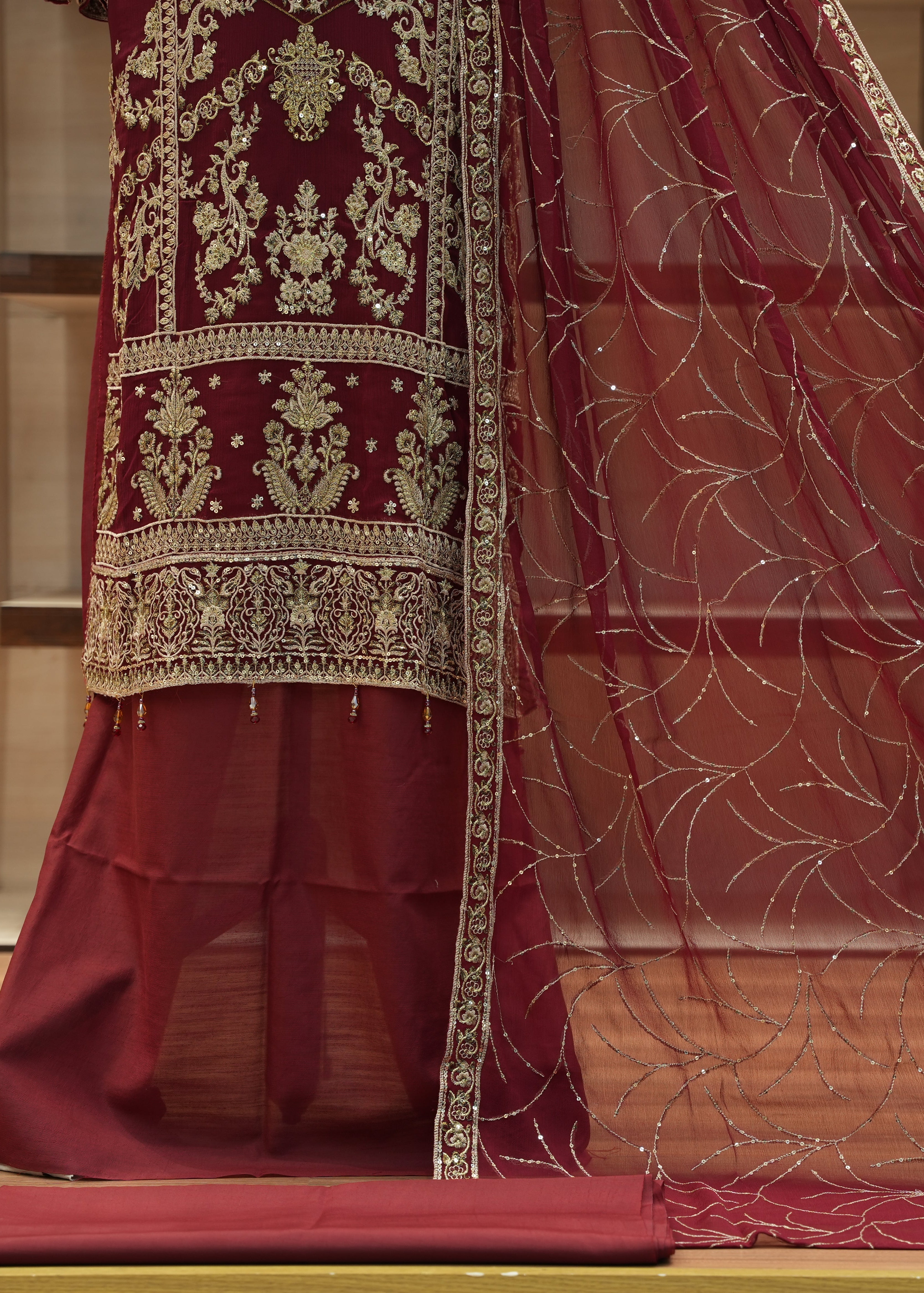Maroon traditional outfit with gold embroidery on a wooden floor.