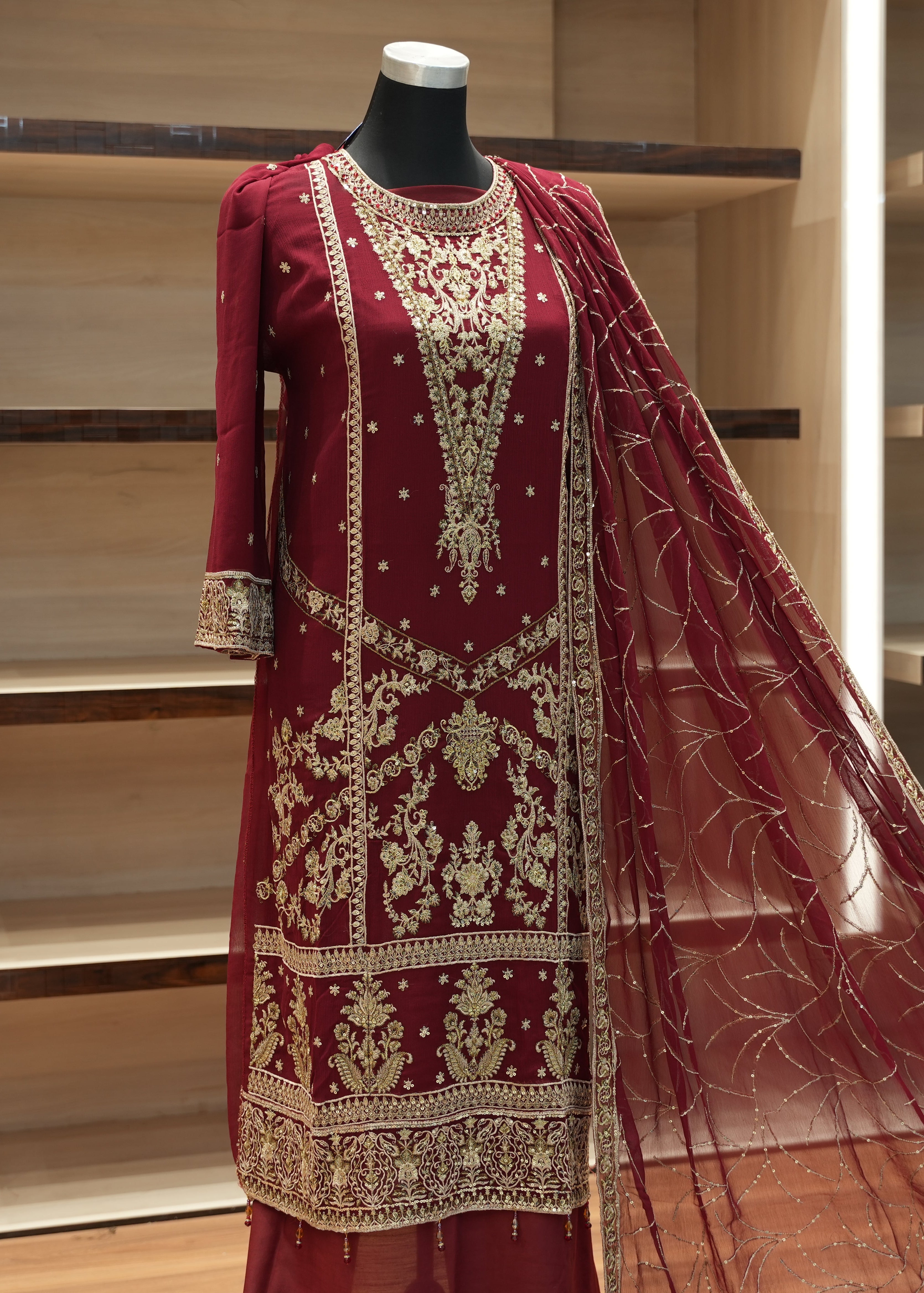 Maroon embroidered traditional outfit on a mannequin against a wooden shelf background