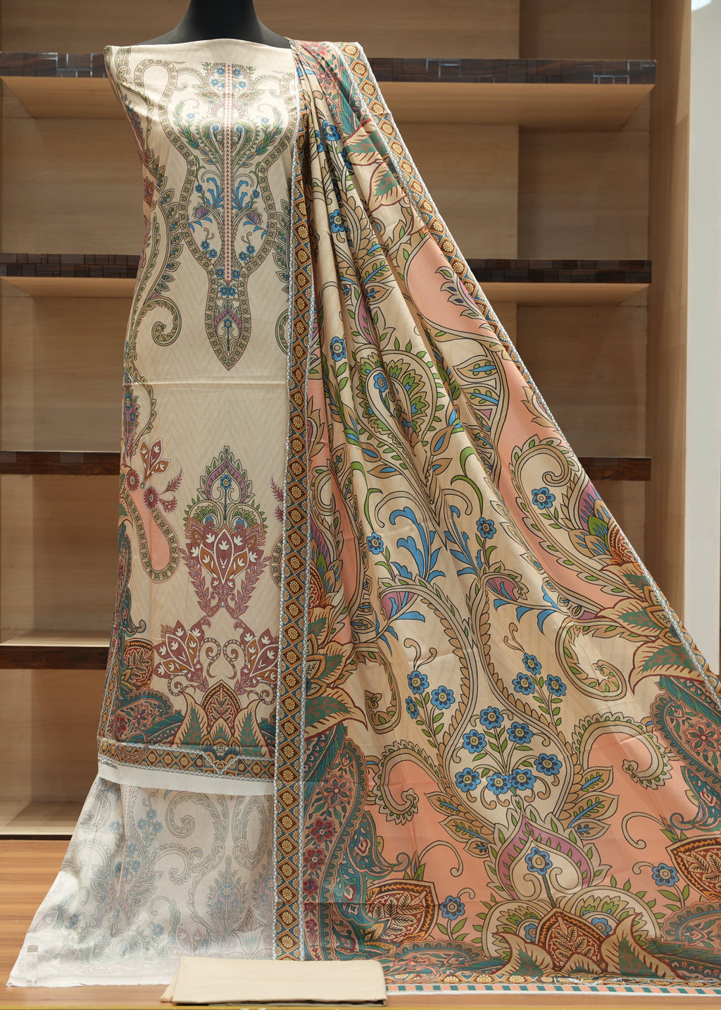 Decorative fabric with intricate patterns on a mannequin against a wooden shelf background