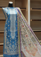 Mannequin wearing a blue embroidered outfit with a patterned shawl against a wooden background