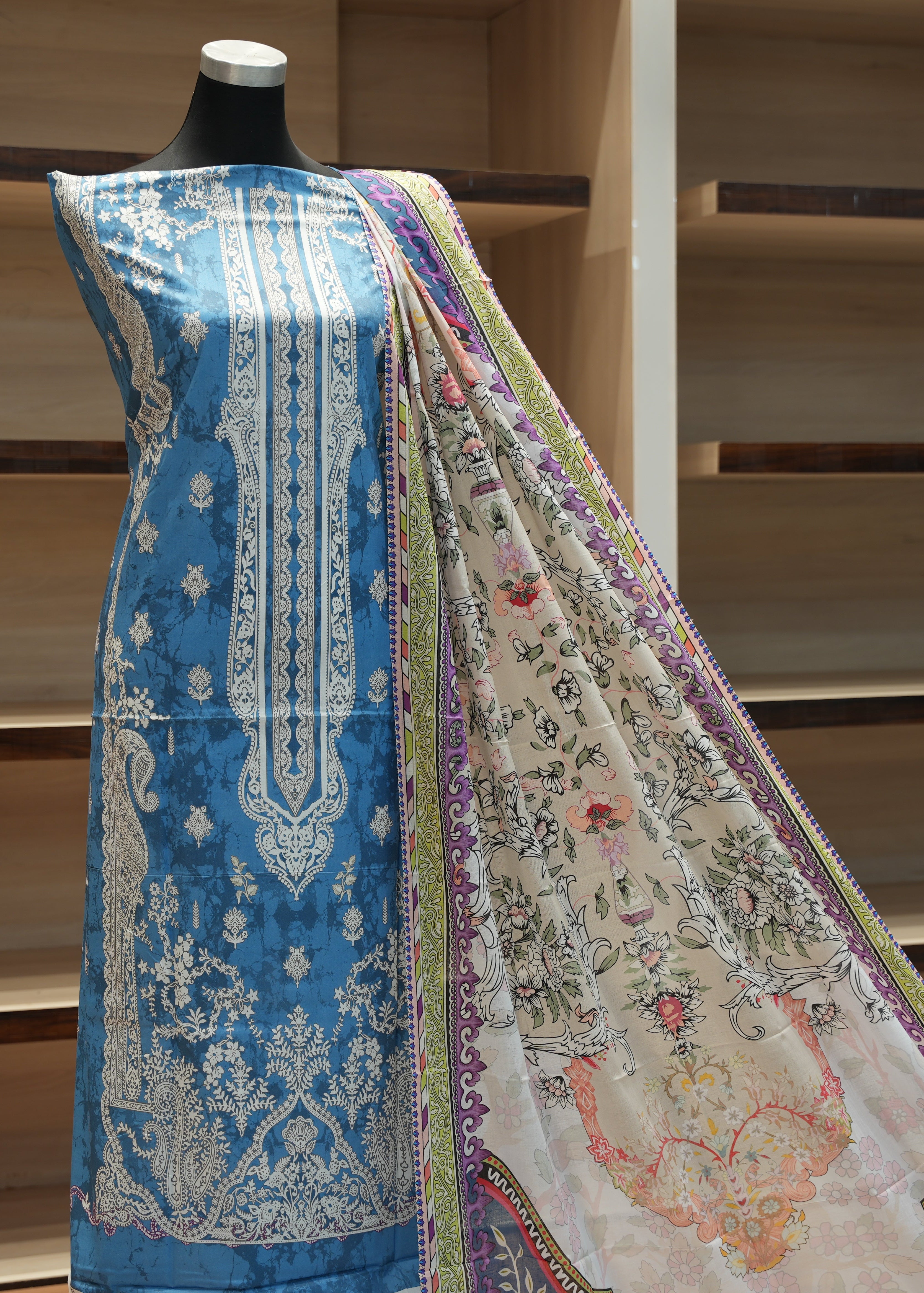 Mannequin wearing a blue embroidered outfit with a patterned shawl against a wooden background