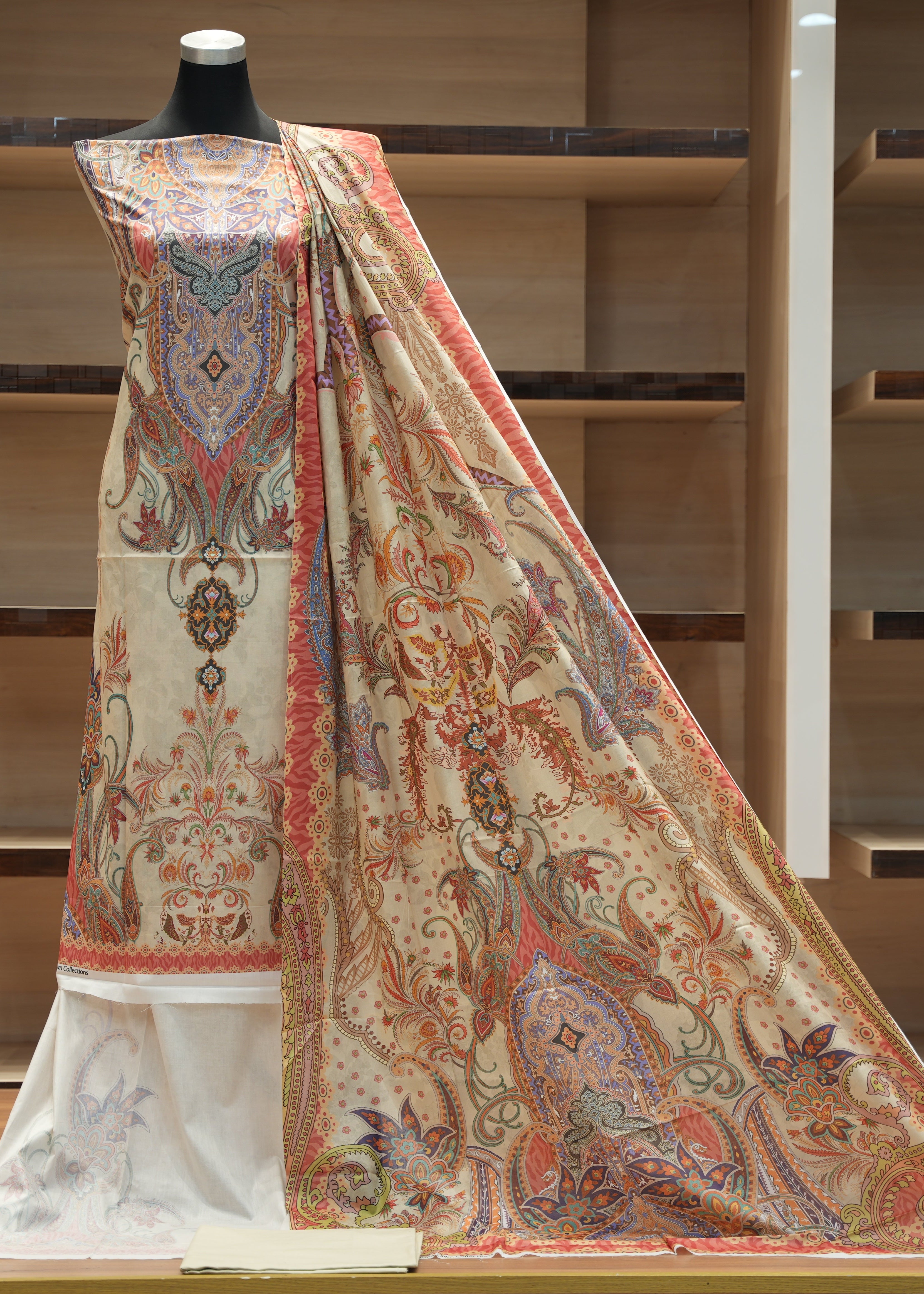 Decorative shawl with intricate patterns on a mannequin against a wooden shelf background