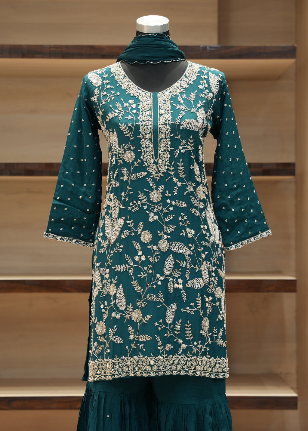 Teal embroidered dress on a mannequin against a wooden background