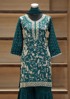 Teal embroidered dress on a mannequin against a wooden background
