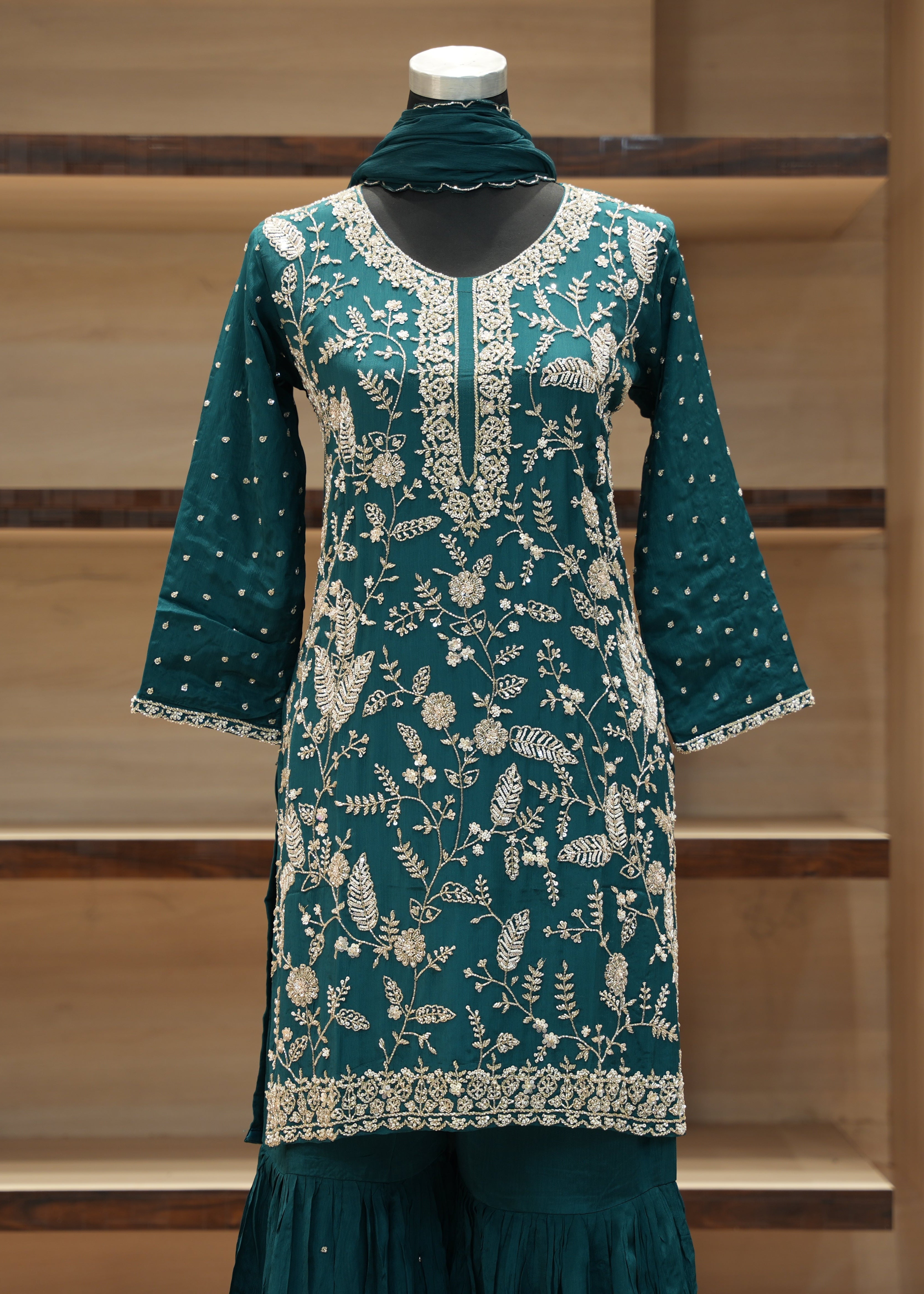 Teal embroidered dress on a mannequin against a wooden background