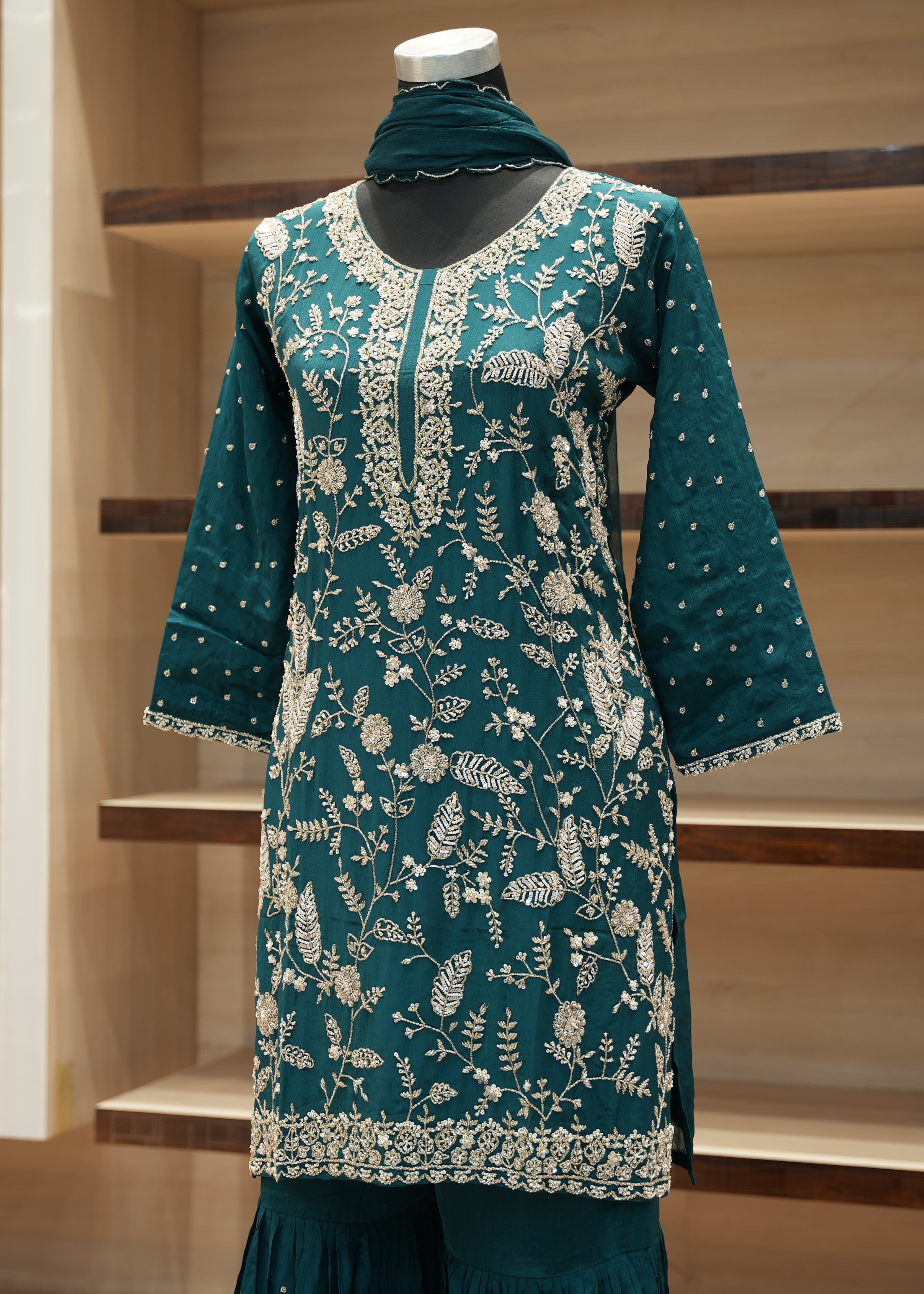 Teal embroidered dress on a mannequin against a wooden shelf background