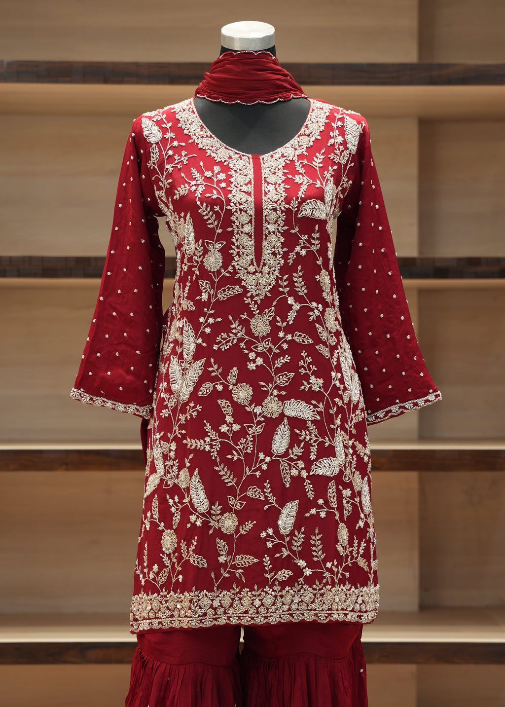 Red embroidered traditional outfit on a mannequin against a wooden shelf background