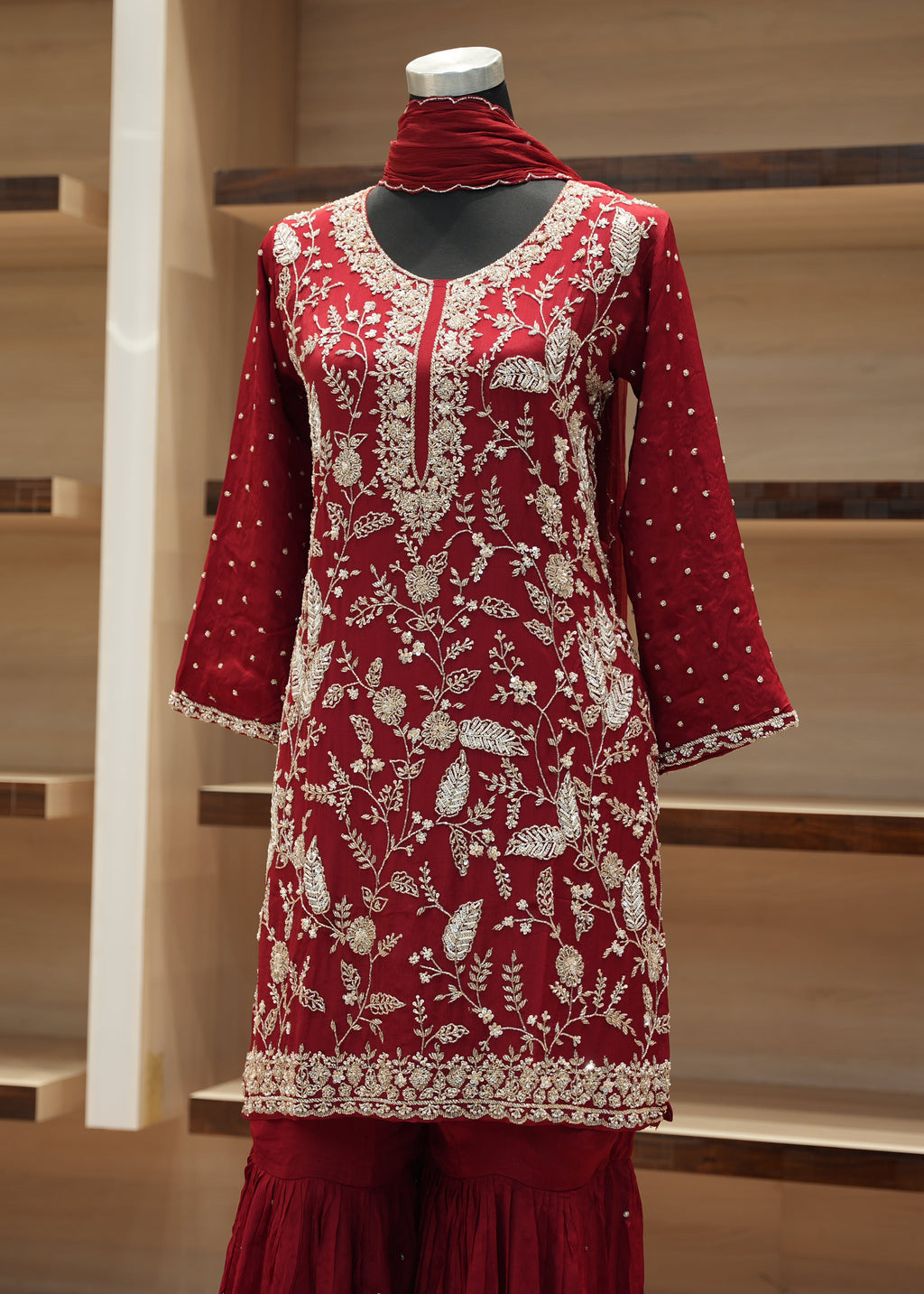 Red embroidered outfit on a mannequin against a wooden staircase background
