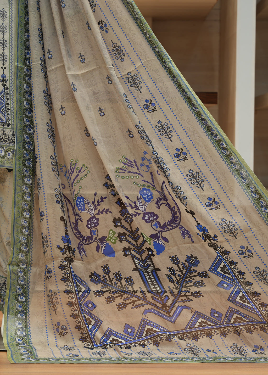 Beige embroidered fabric with blue and green patterns on a wooden floor.
