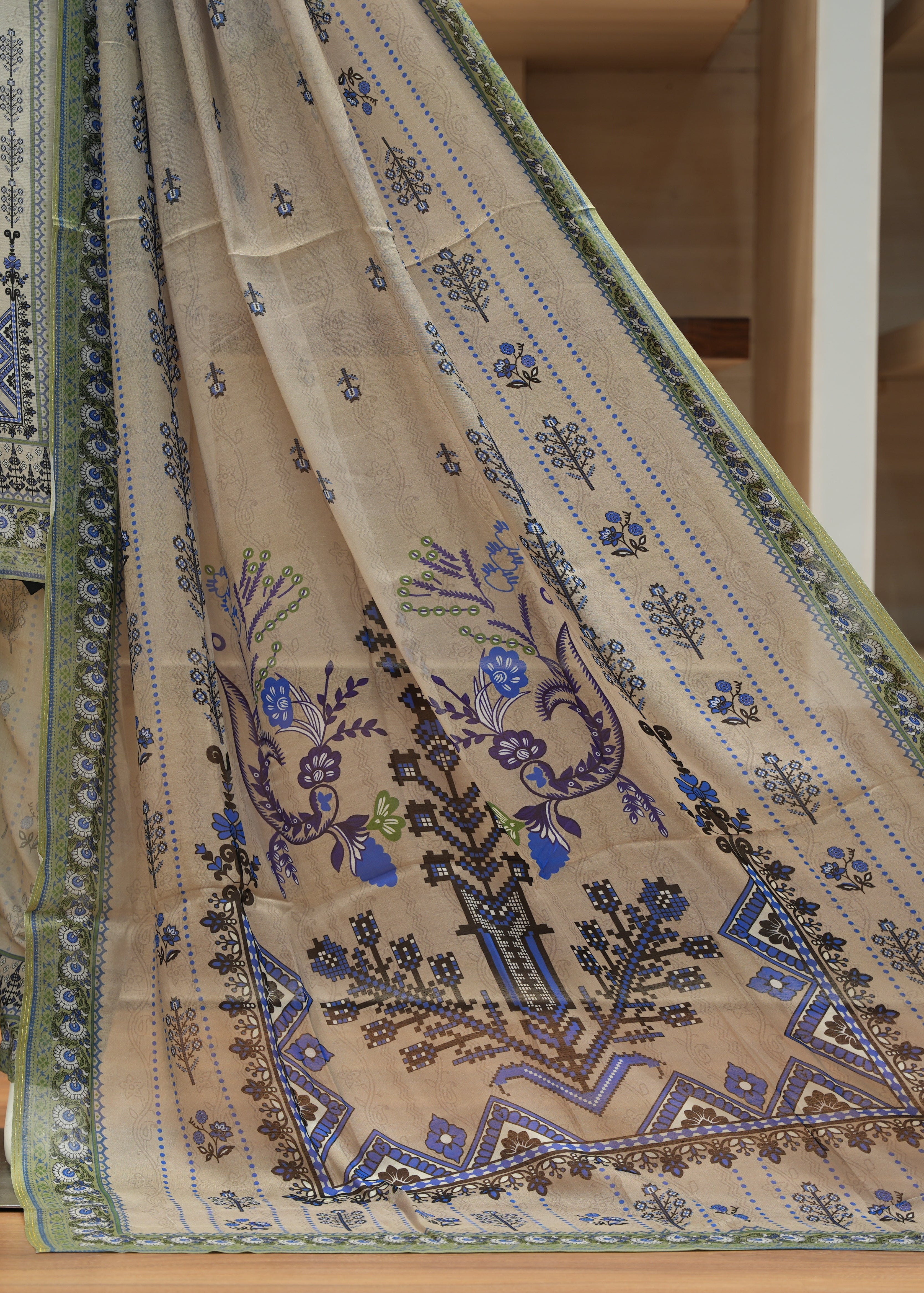 Beige embroidered fabric with blue and green patterns on a wooden floor.