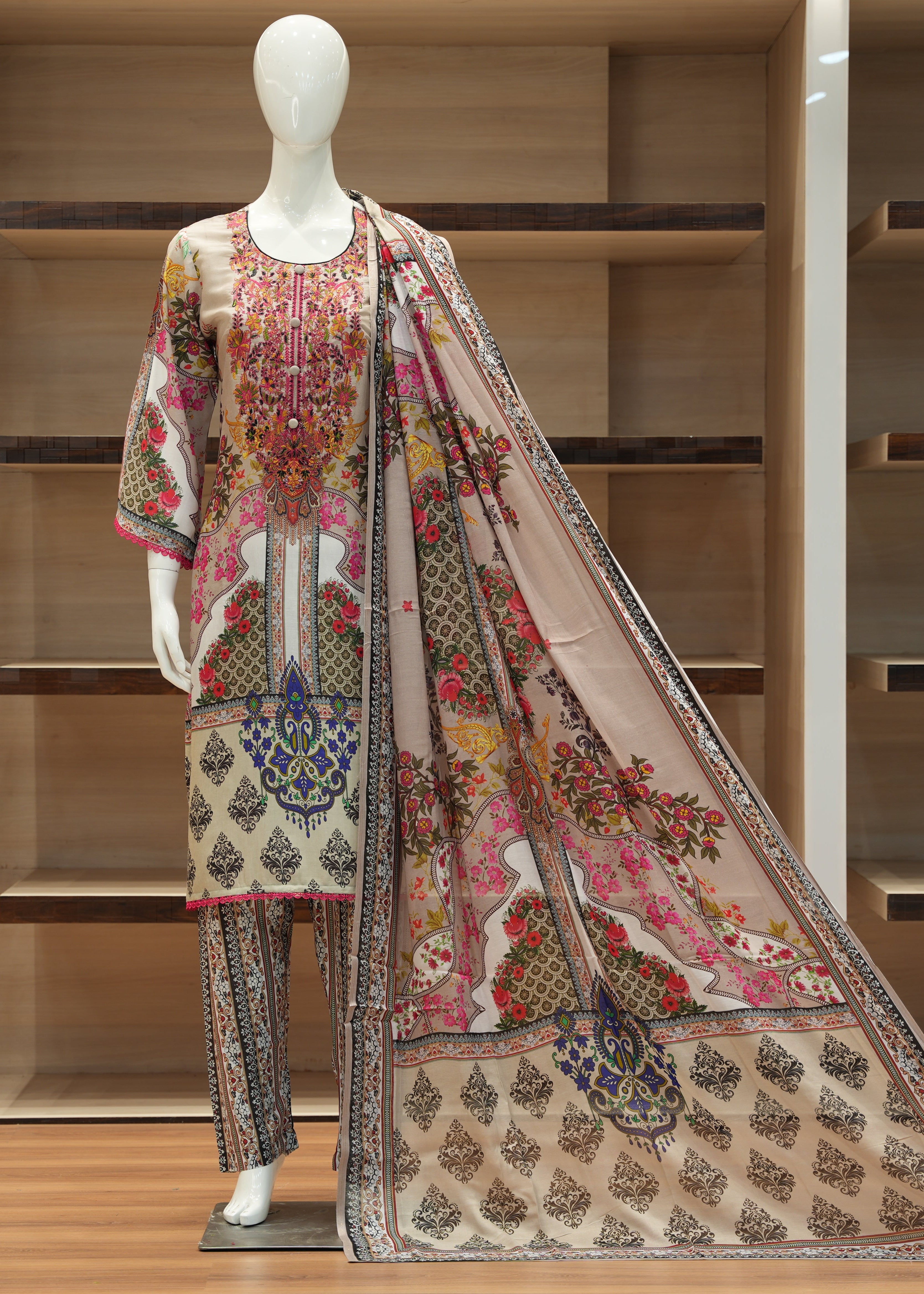 Mannequin wearing a colorful embroidered outfit with a patterned scarf against a wooden shelf background.