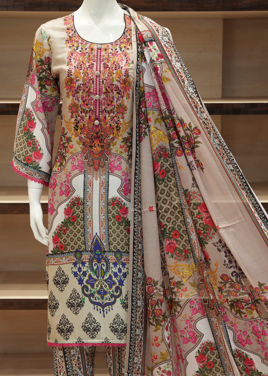 Colorful embroidered outfit with a matching shawl on a mannequin against a wooden shelf background.