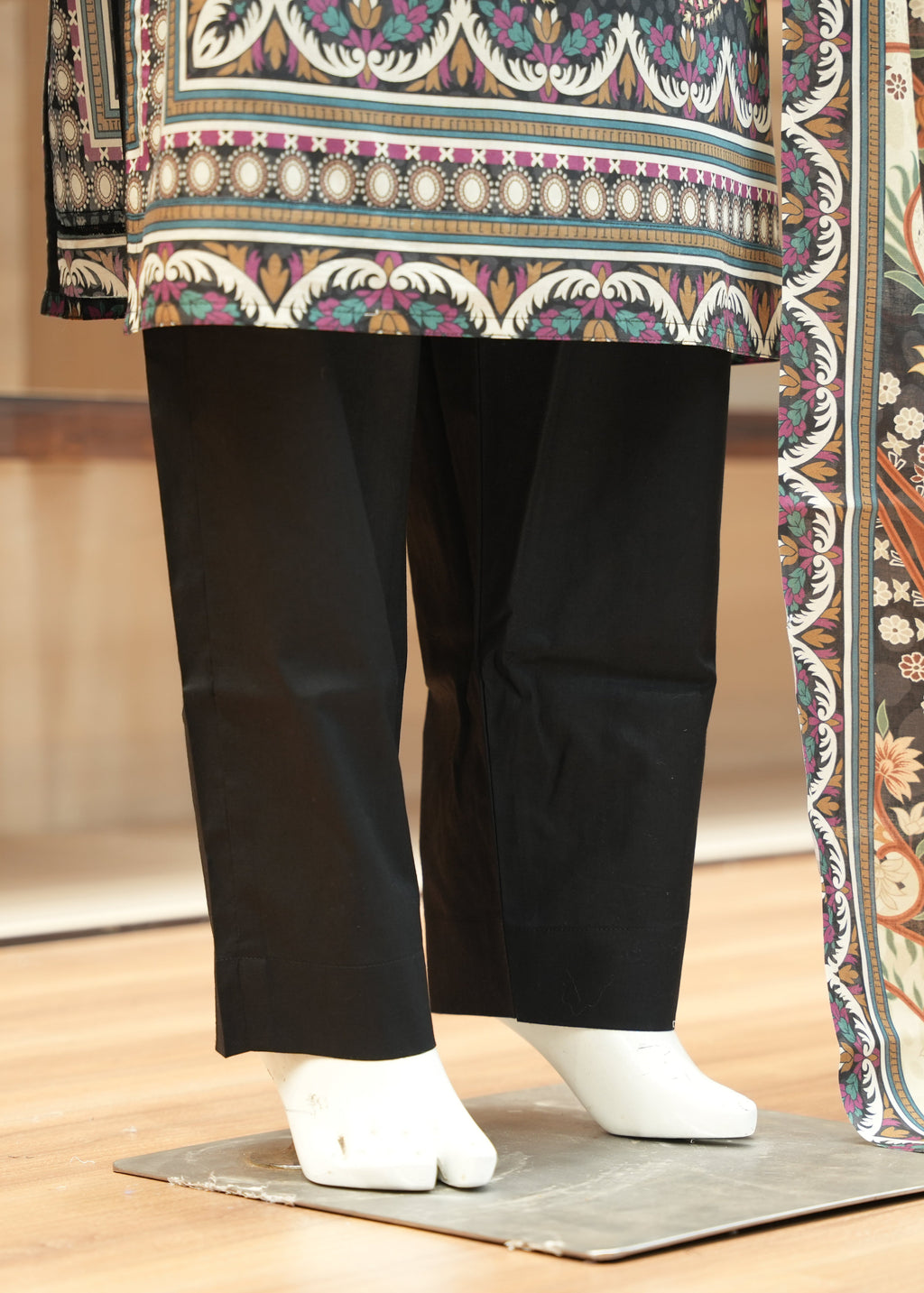 Traditional outfit with a colorful top and black pants on a wooden floor.