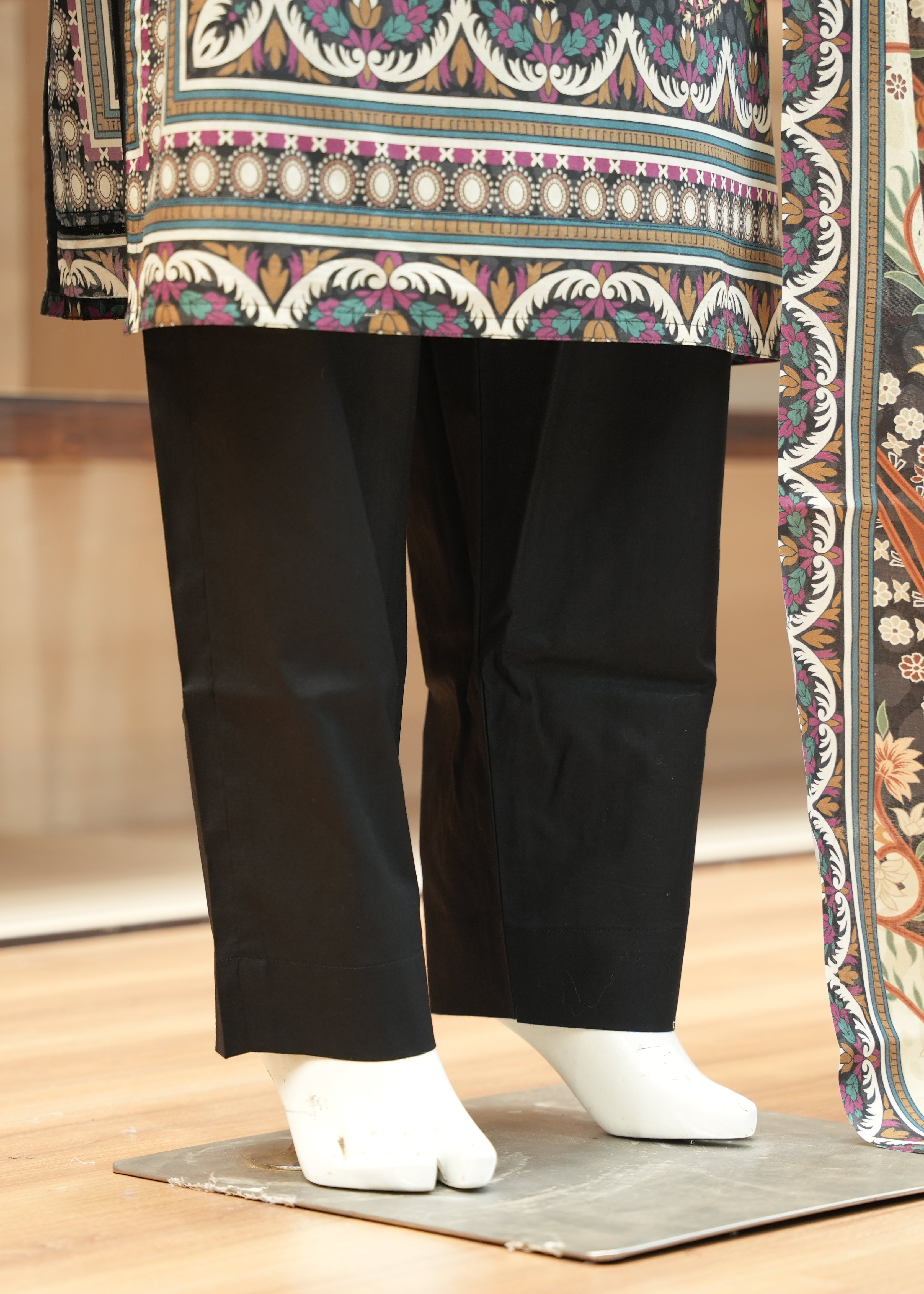 Traditional outfit with a colorful top and black pants on a wooden floor.