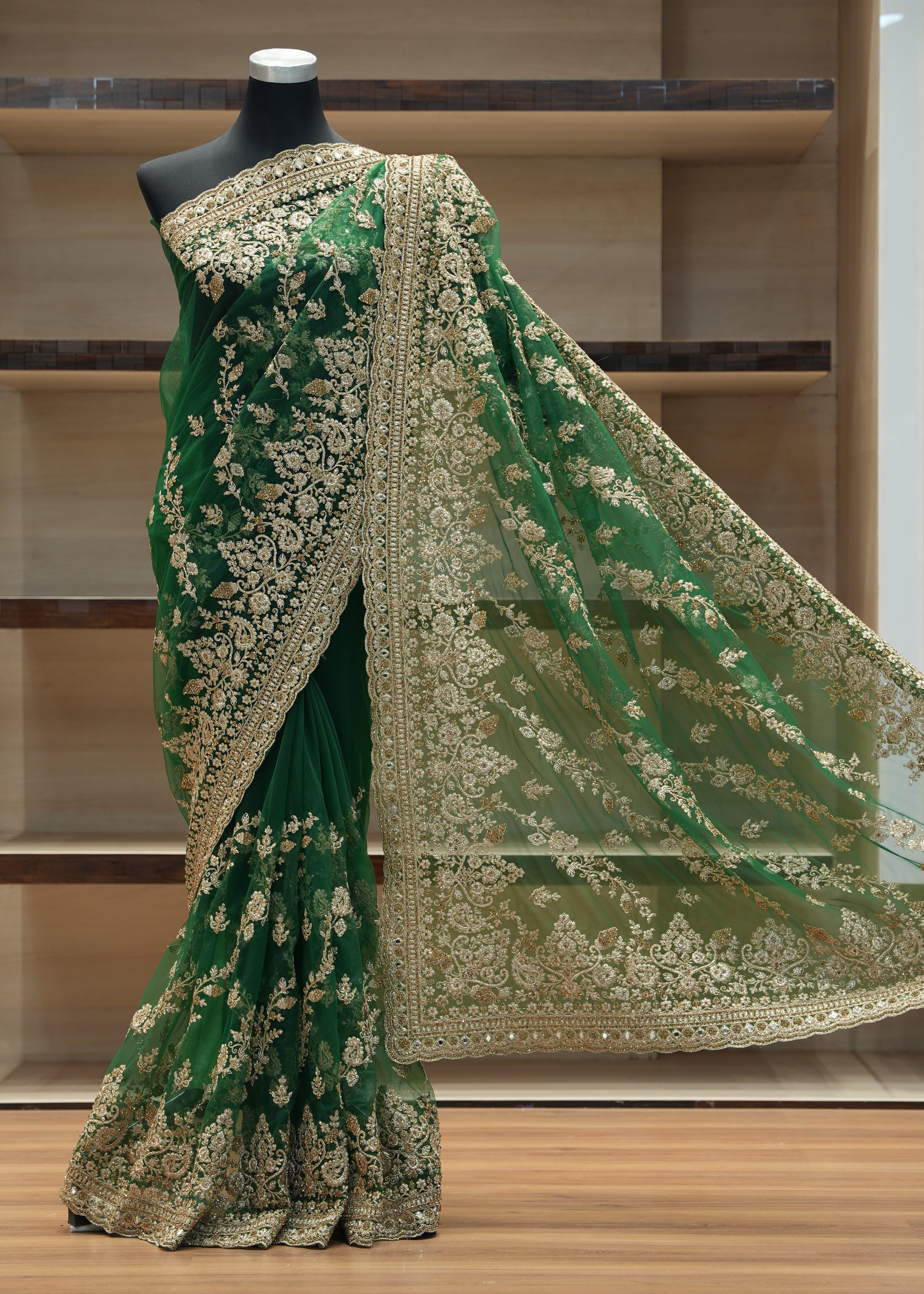 Green embroidered saree with gold details on a mannequin against a wooden background