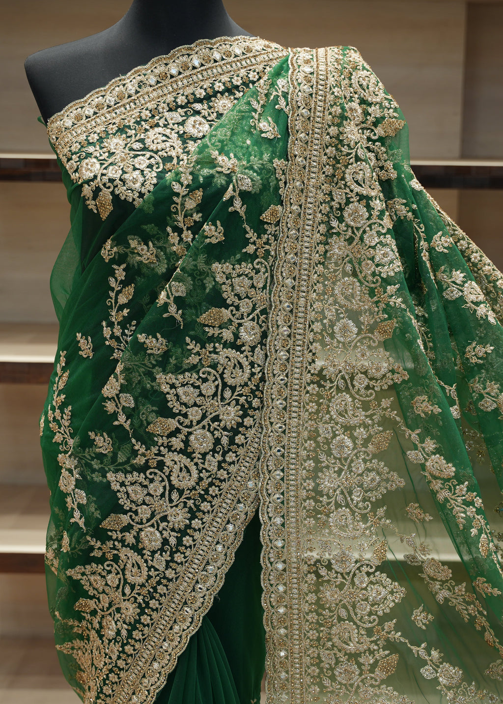 Green saree with intricate gold embroidery on a mannequin against a neutral background