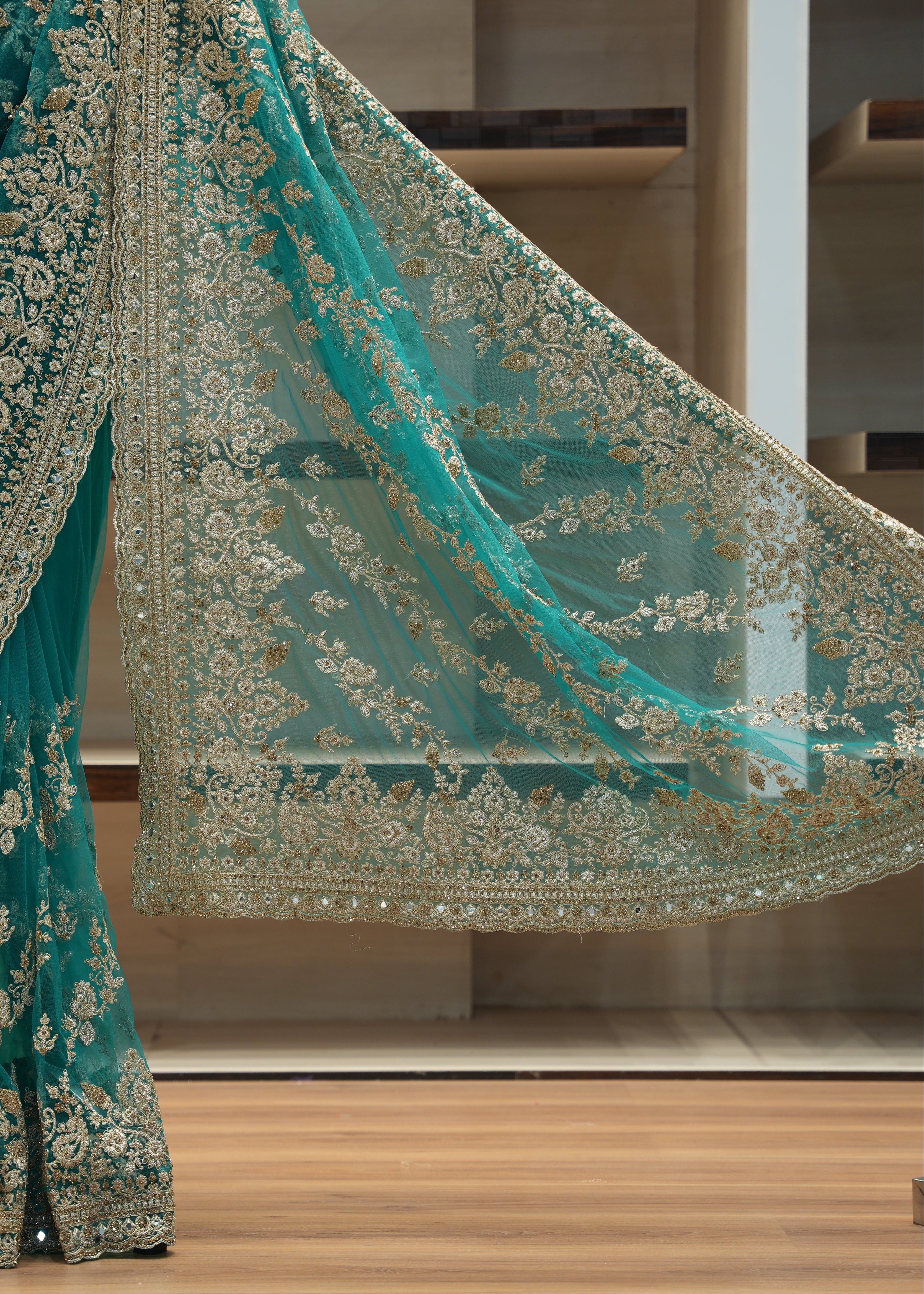 Teal saree with gold embroidery on a wooden floor