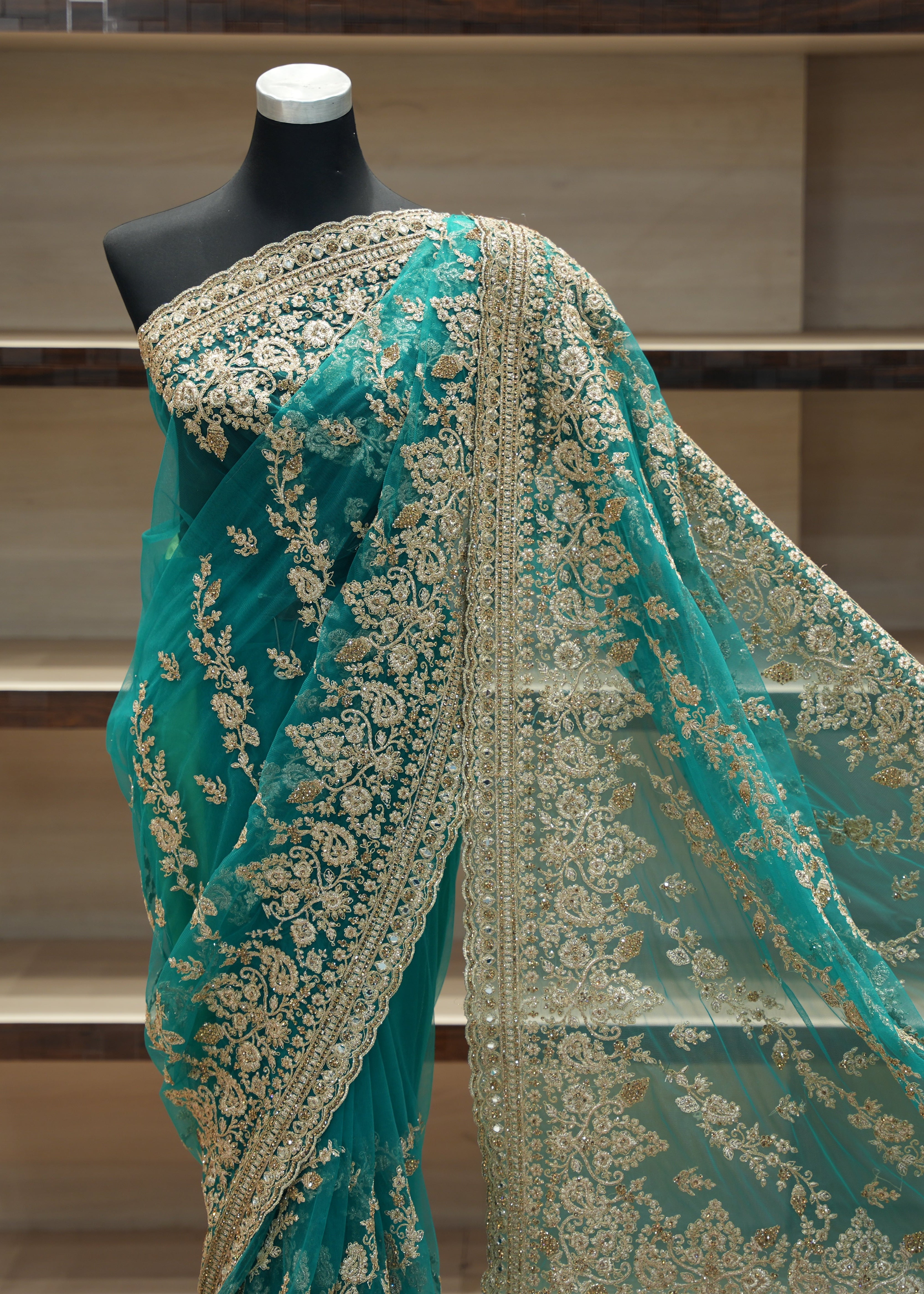 Teal saree with gold embroidery on a mannequin against a neutral background