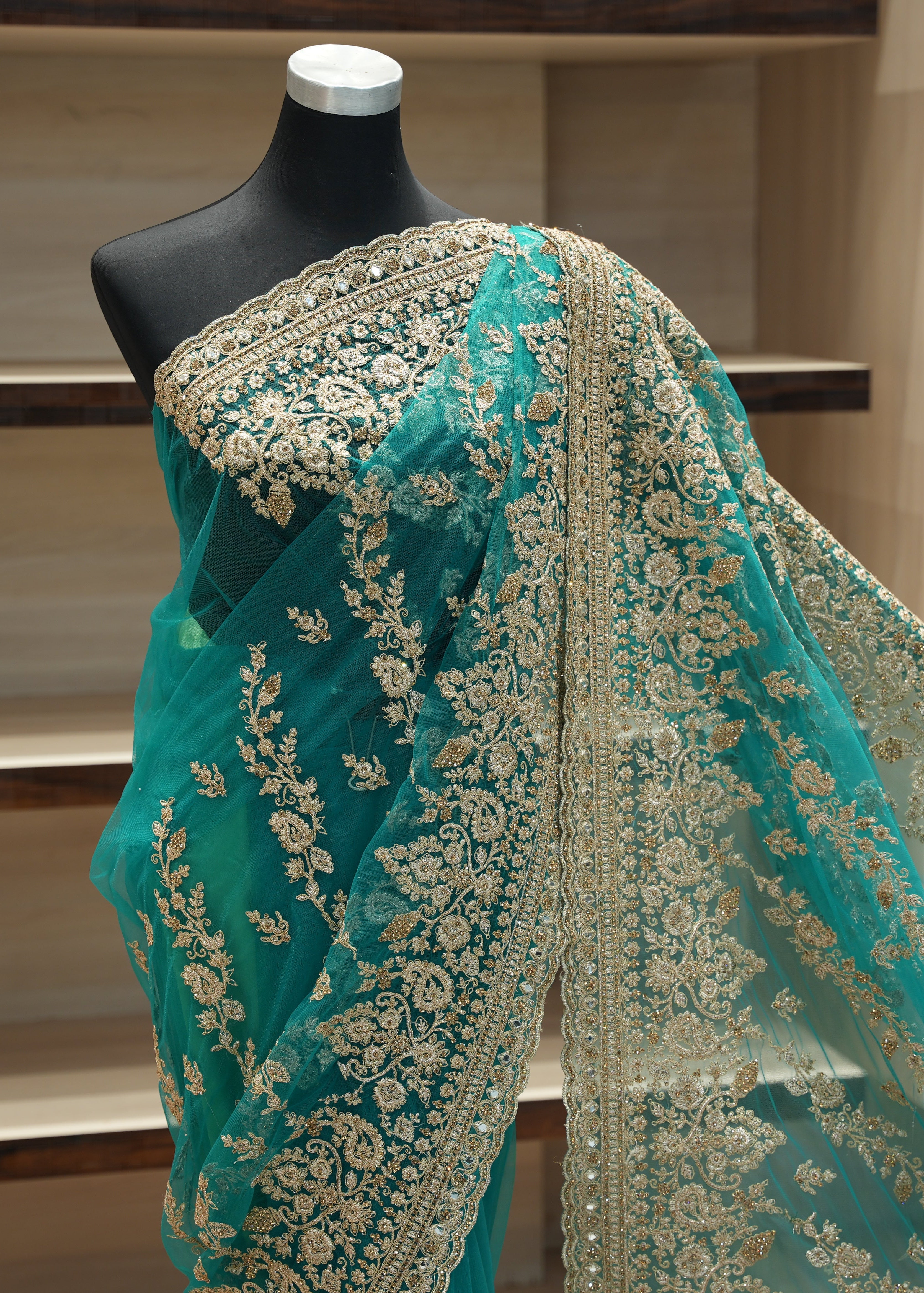 Teal saree with gold embroidery on a mannequin against a neutral background