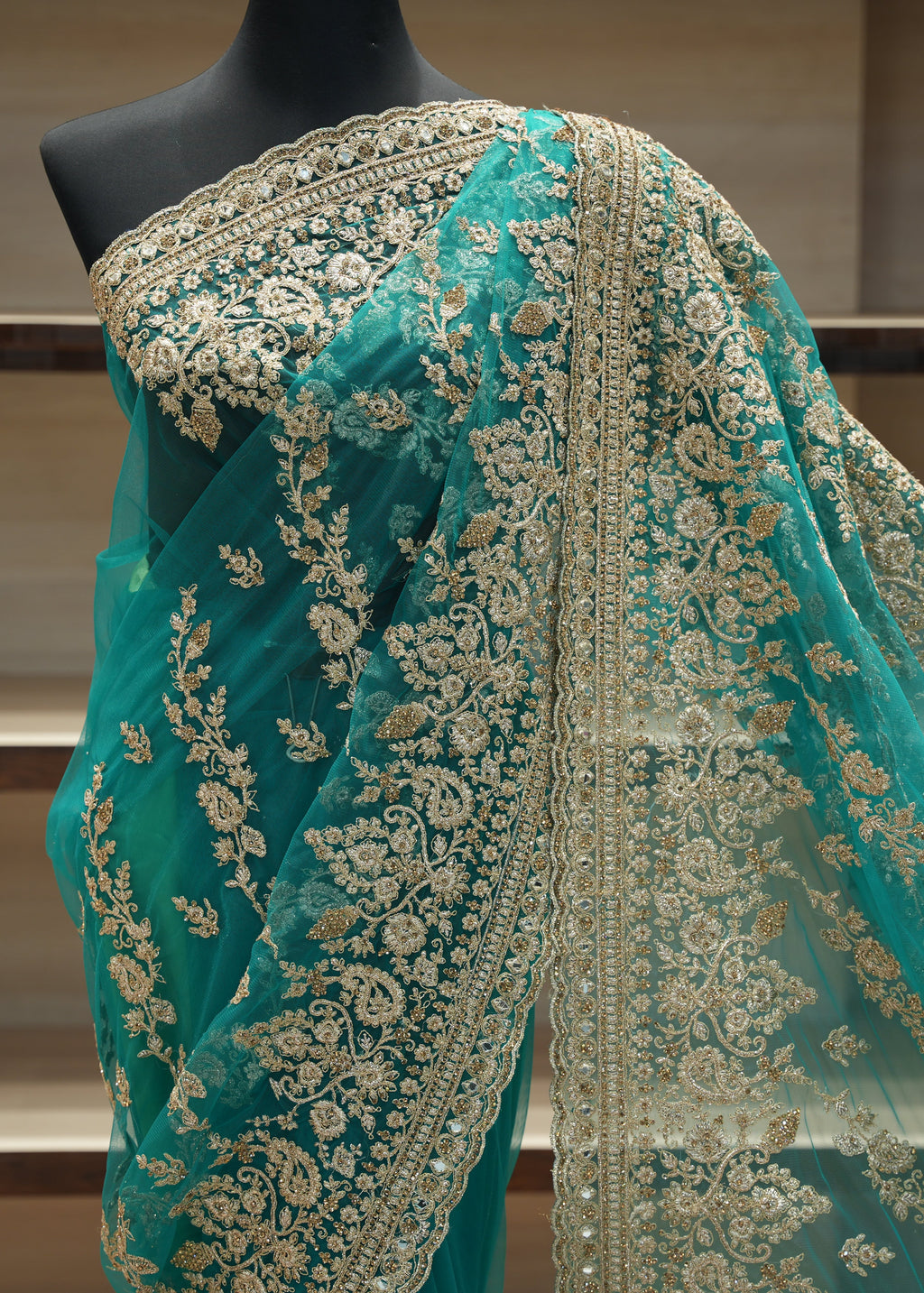 Teal saree with gold embroidery on a mannequin against a neutral background