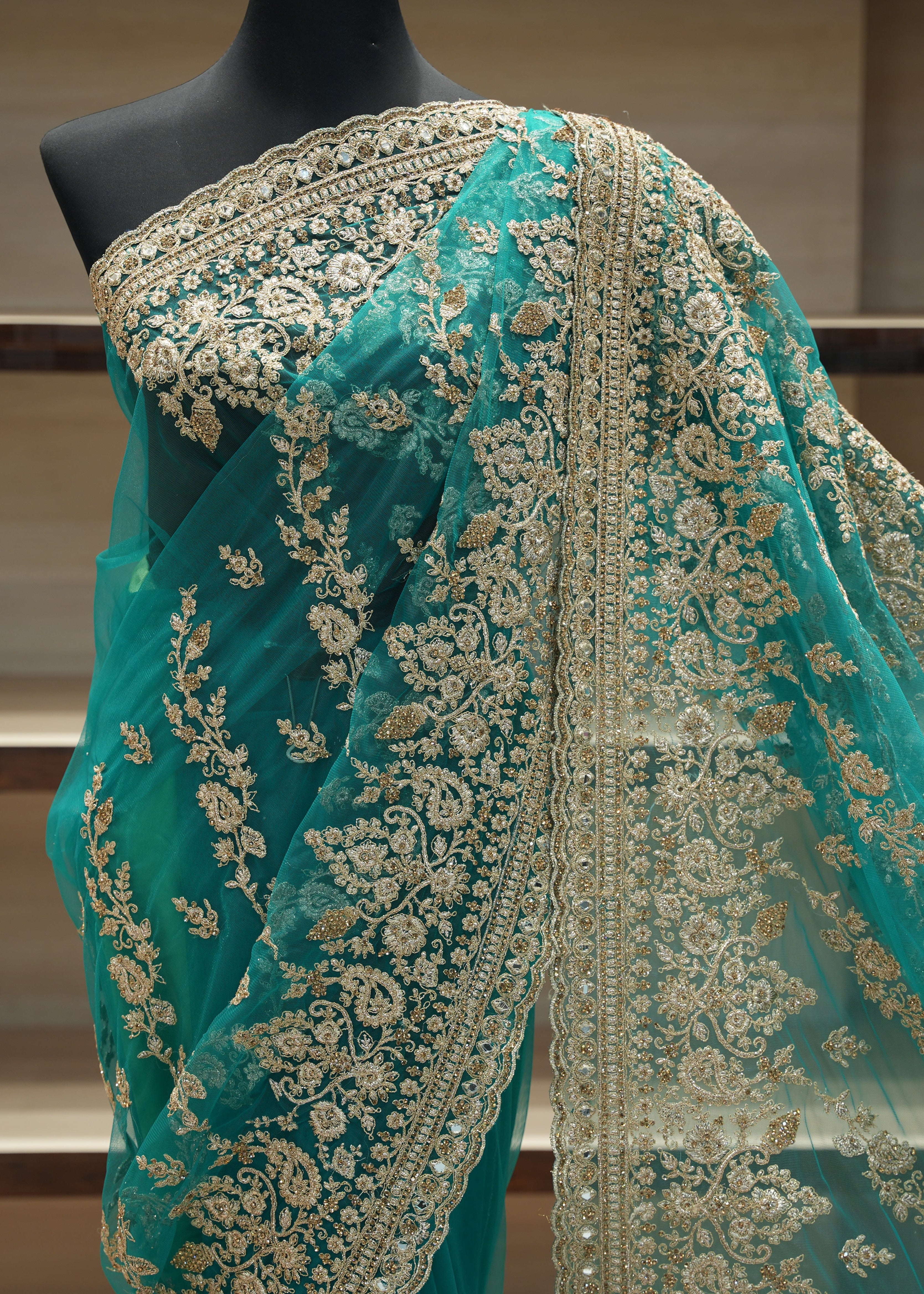 Teal saree with gold embroidery on a mannequin against a neutral background