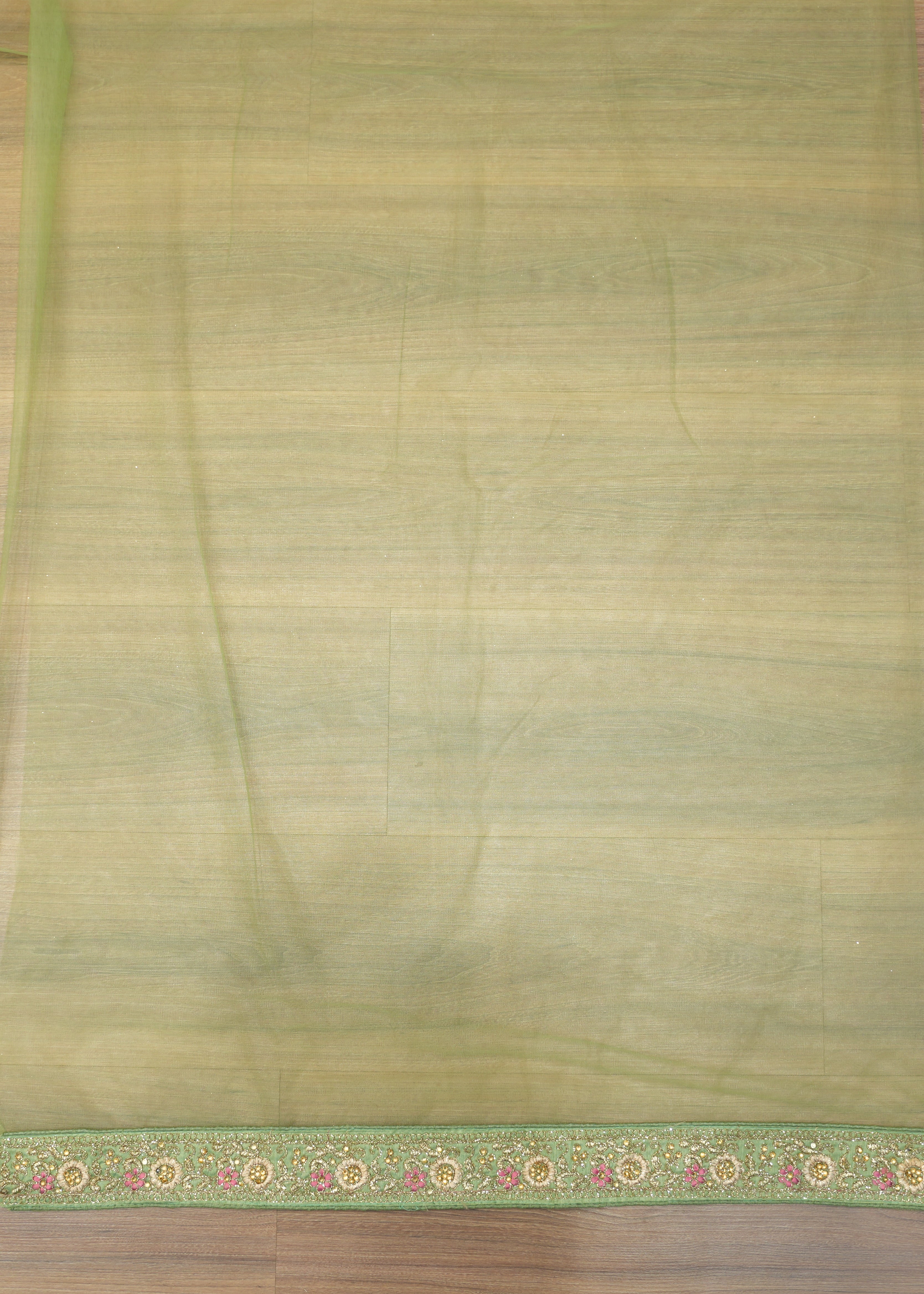 Green saree with a floral border on a wooden floor