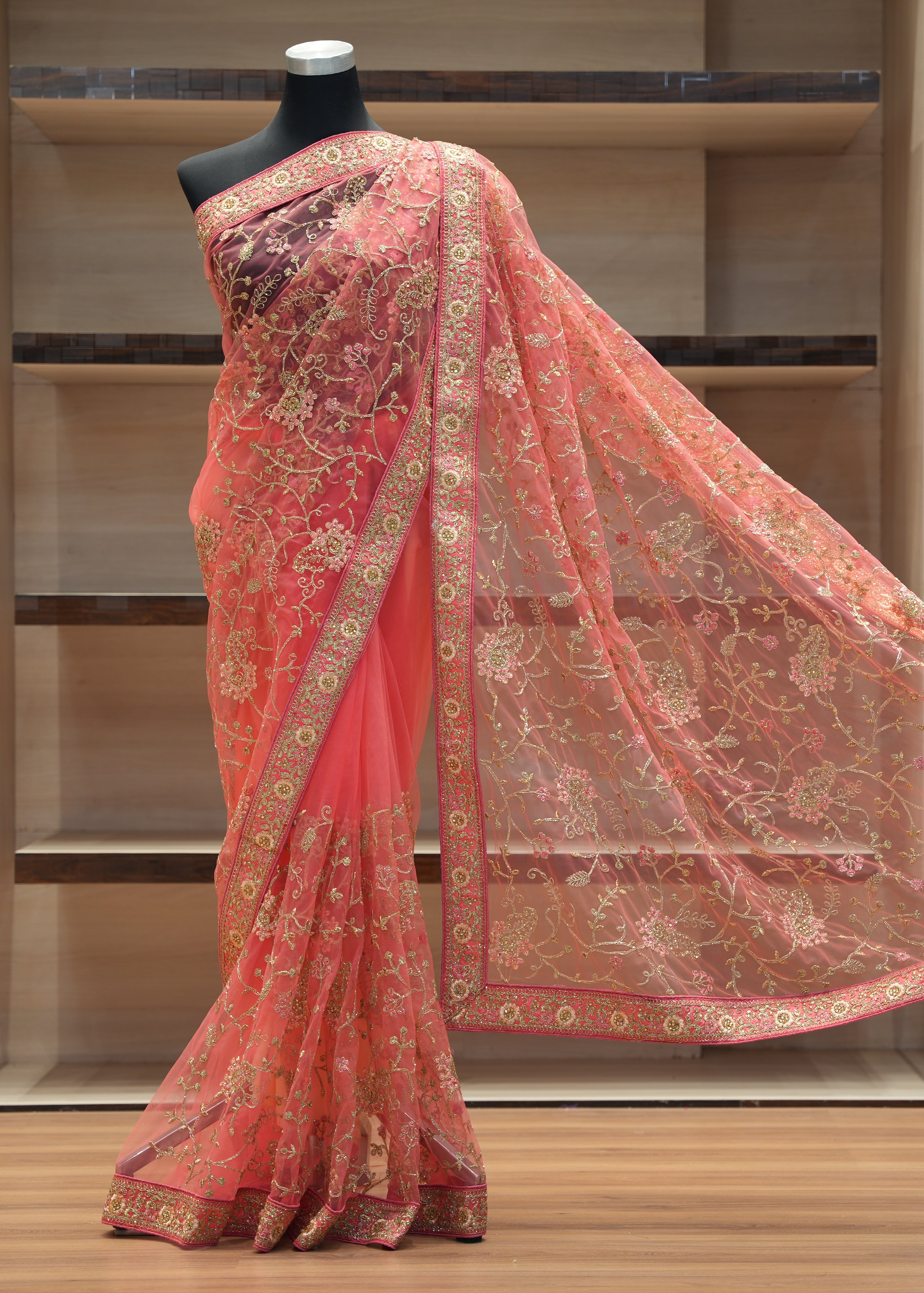 Pink saree with gold patterns on a mannequin against a wooden background