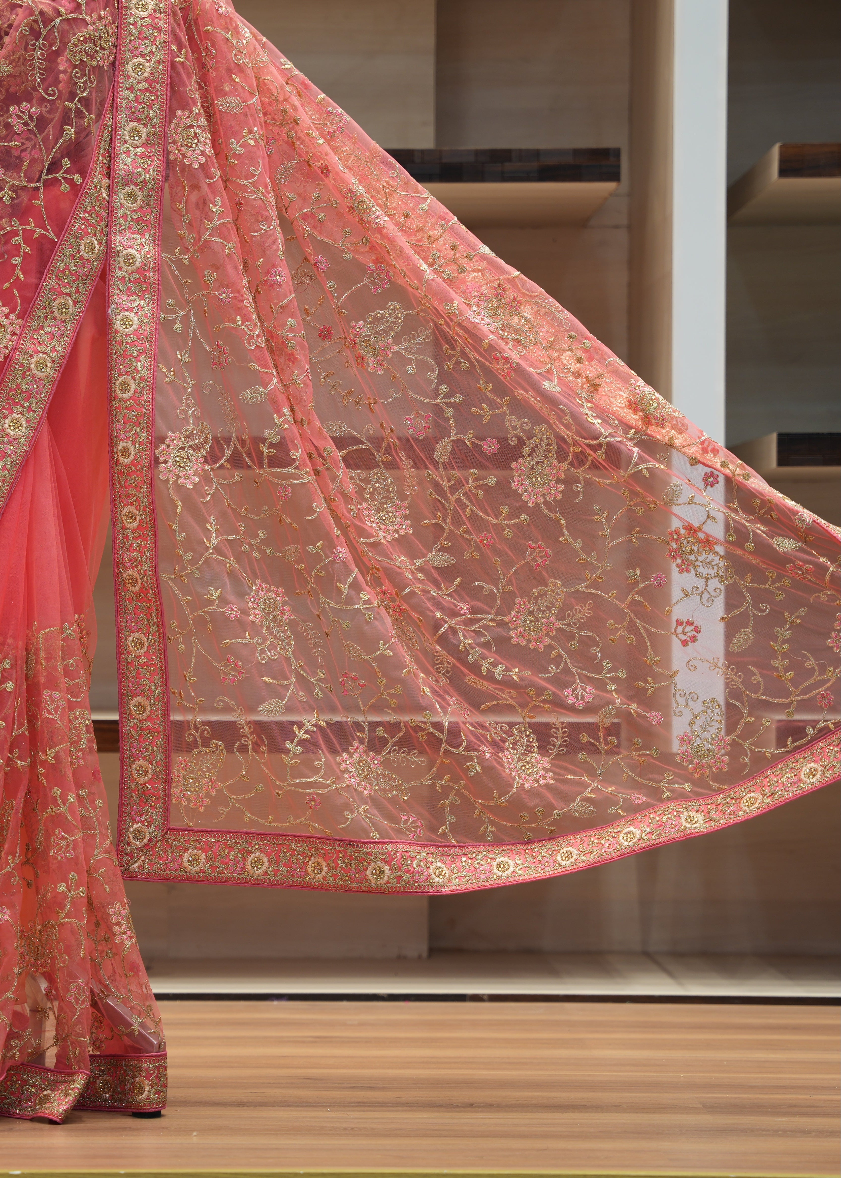Coral pink saree with gold embroidery on a wooden floor