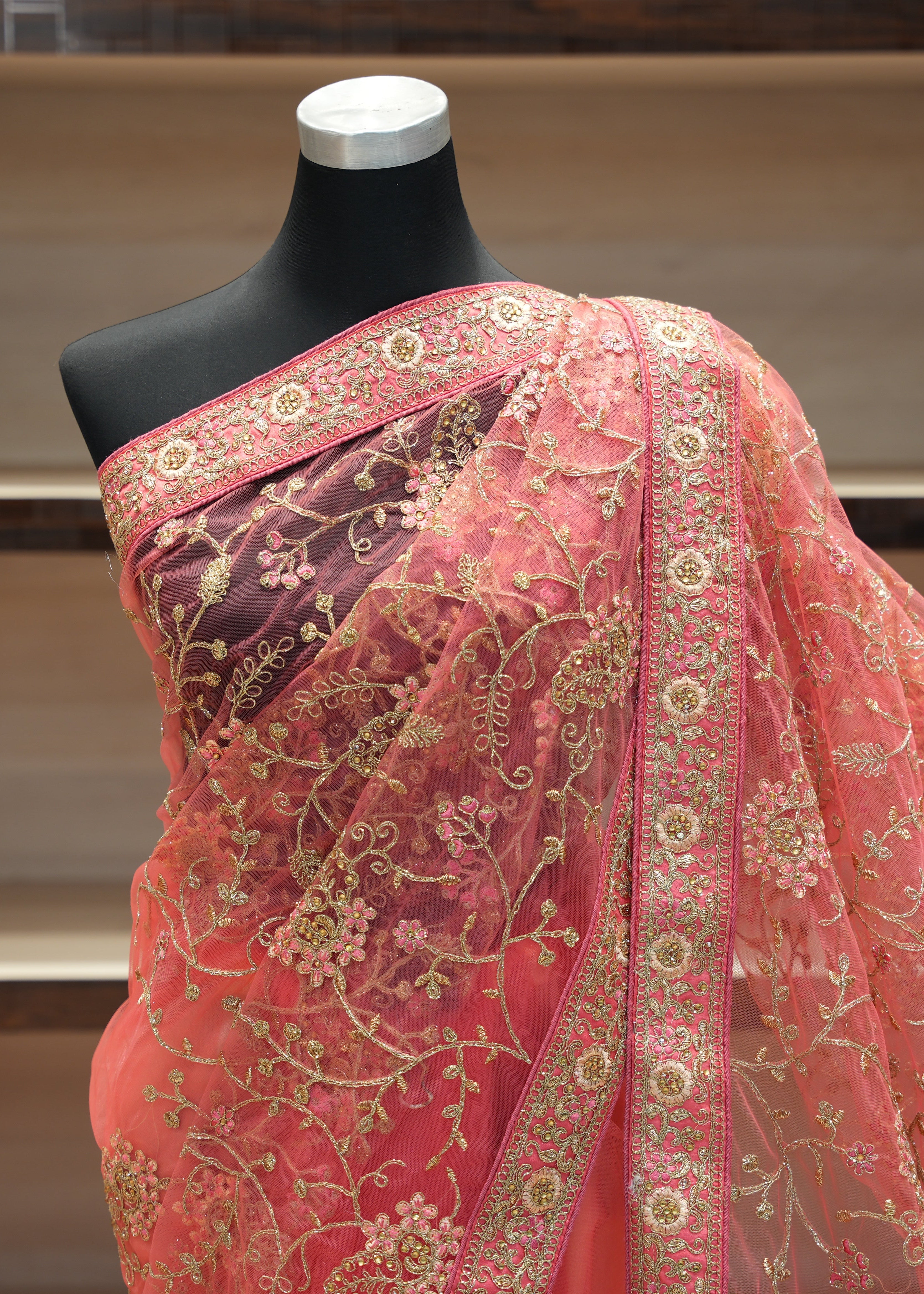 Pink saree with intricate gold embroidery on a mannequin against a neutral background