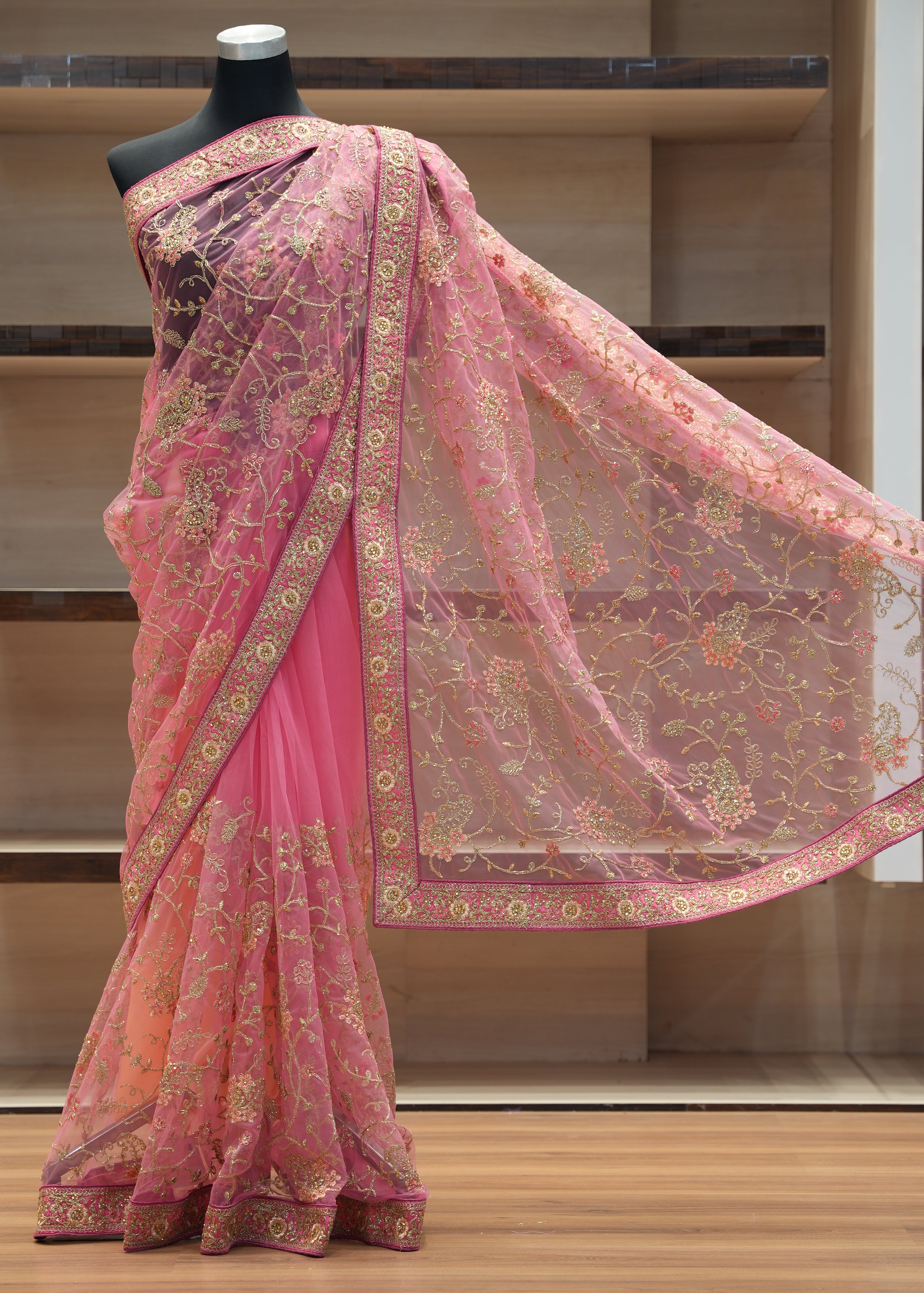 Pink saree with gold patterns on a mannequin against a wooden background