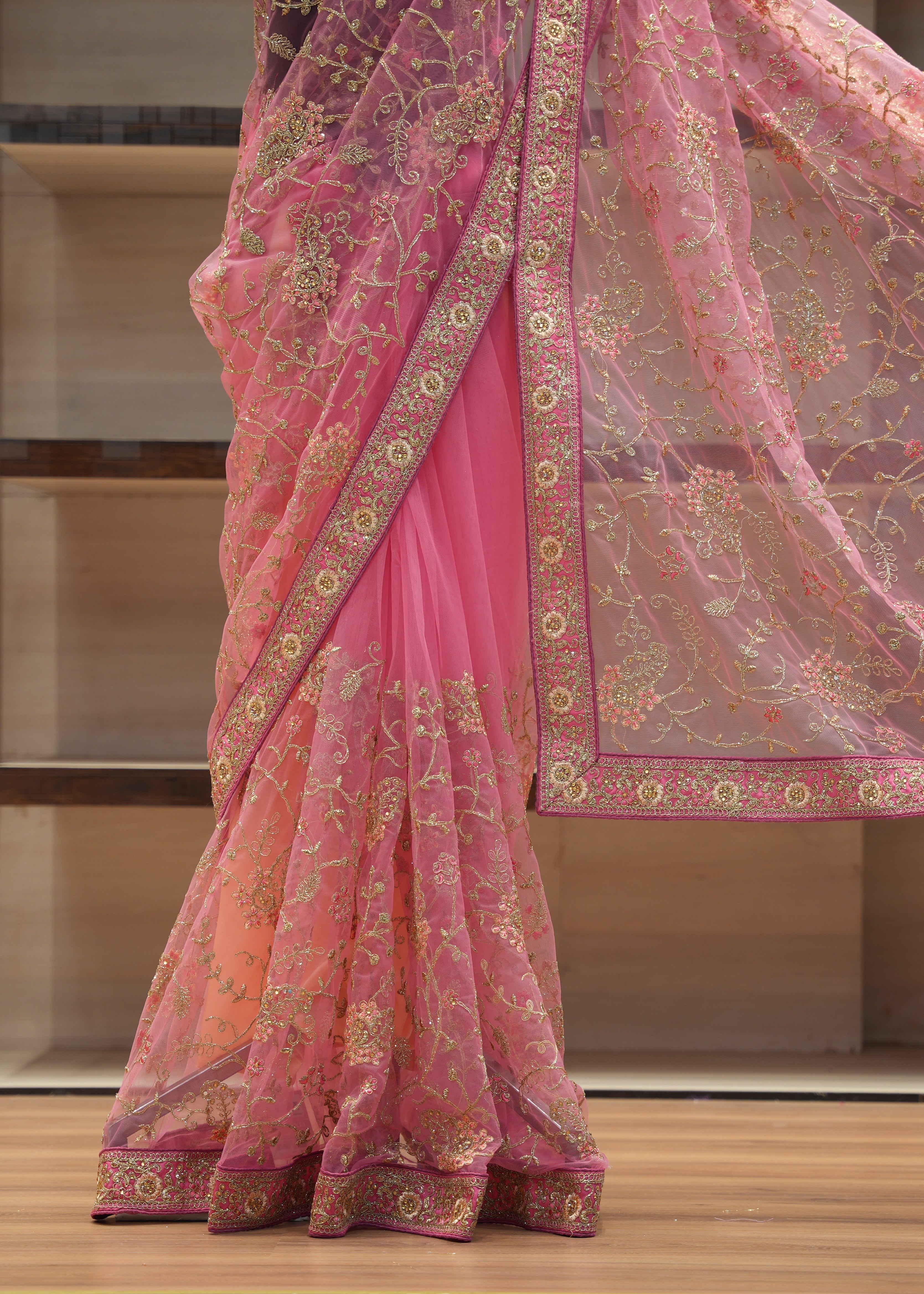 Pink saree with intricate gold embroidery on a wooden floor.