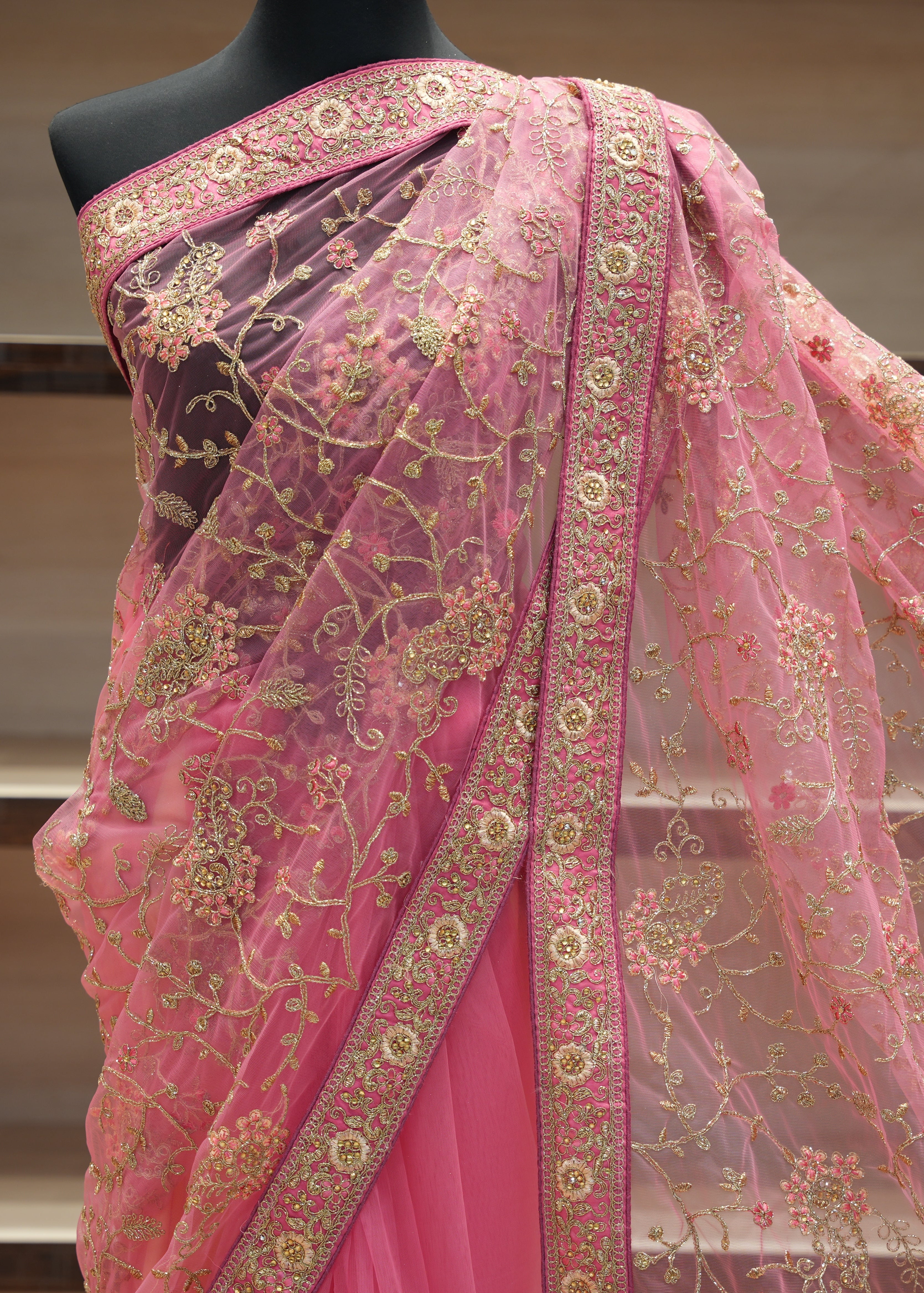 Pink saree with gold embroidery on a mannequin against a neutral background