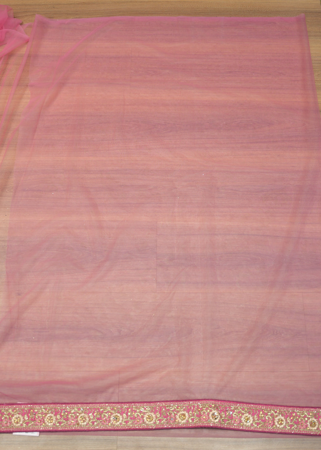 Pink sheer fabric with decorative border on a wooden surface