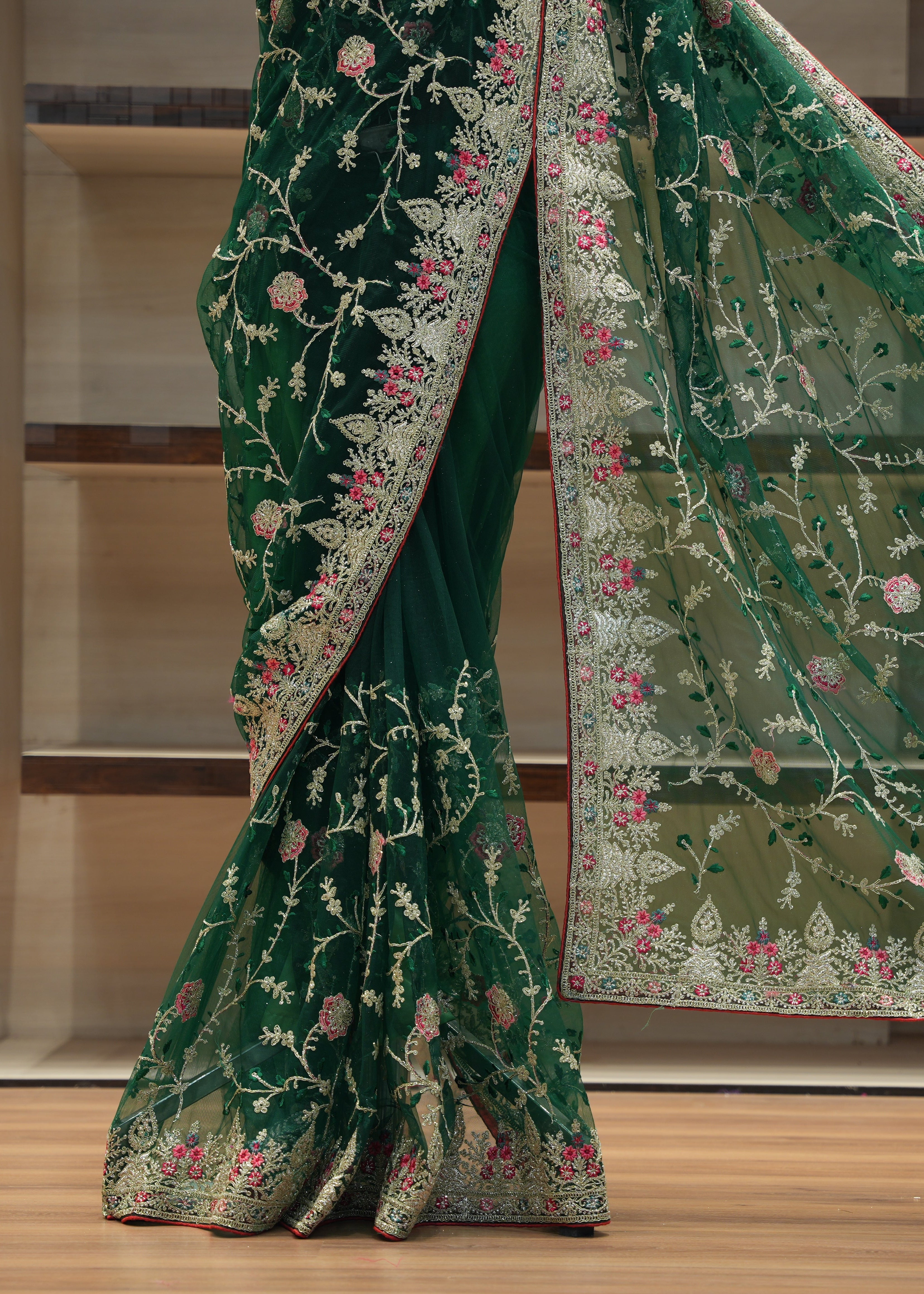 Green embroidered saree with a floral pattern on a wooden floor.