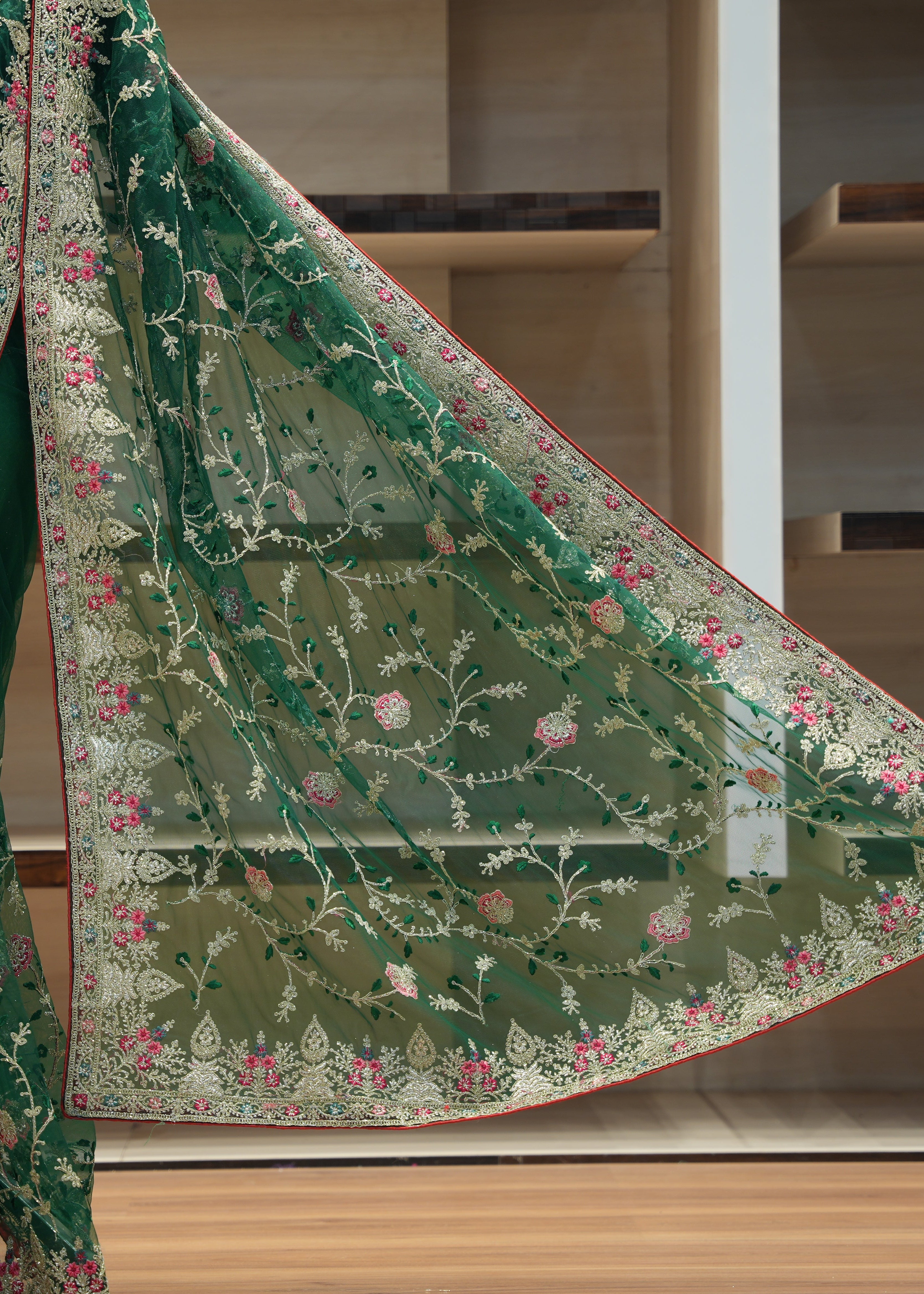 Green embroidered saree with floral patterns on a wooden floor.