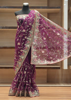 A purple georgette saree with intricate gold, silver, and pink floral embroidery, displayed on a black mannequin torso in front of wooden shelving.