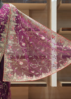 A deep purple saree with an elaborate gold, beige, and pink floral embroidered border, displayed on a mannequin in a boutique setting.