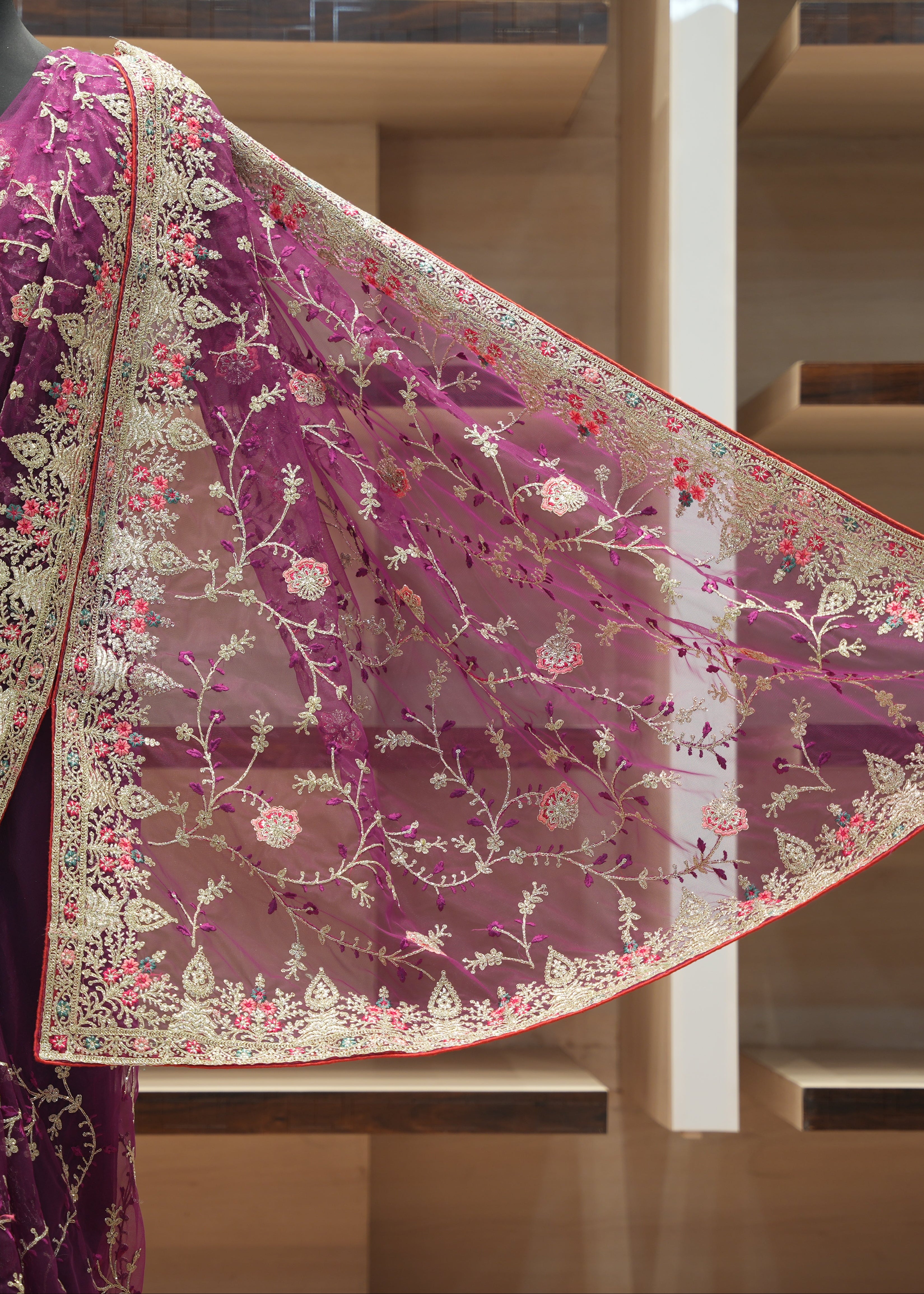 A deep purple saree with an elaborate gold, beige, and pink floral embroidered border, displayed on a mannequin in a boutique setting.