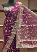 A deep purple velvet saree with intricate beige floral embroidery and a matching sheer net dupatta, displayed on a black mannequin torso against a wooden background.