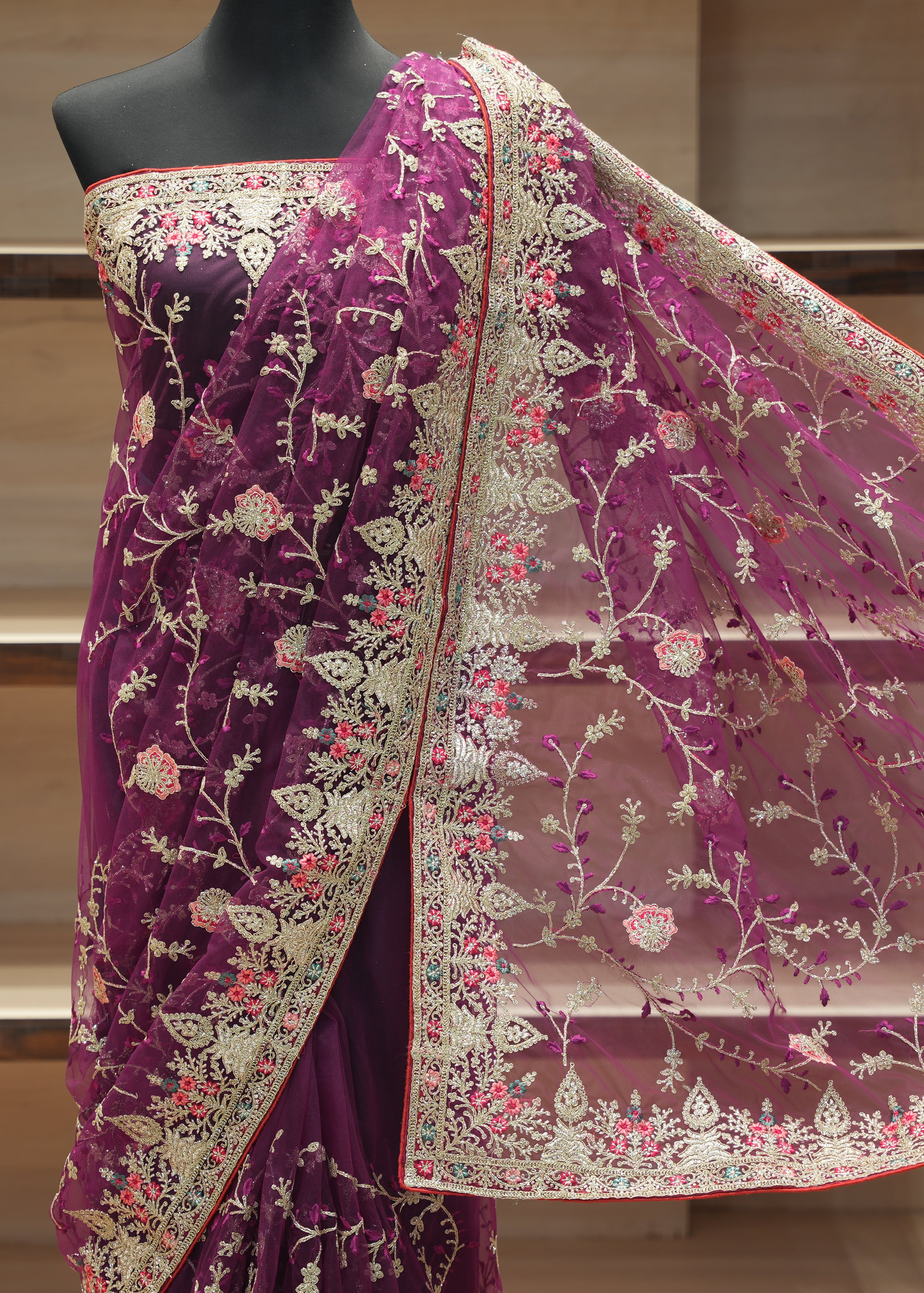 A deep purple velvet saree with intricate beige floral embroidery and a matching sheer net dupatta, displayed on a black mannequin torso against a wooden background.