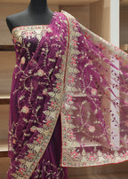 A deep purple georgette saree with intricate beige floral embroidery and a red border, draped on a black mannequin torso. The matching sheer net dupatta is spread out to the right, showcasing the detailed embroidery and border design.