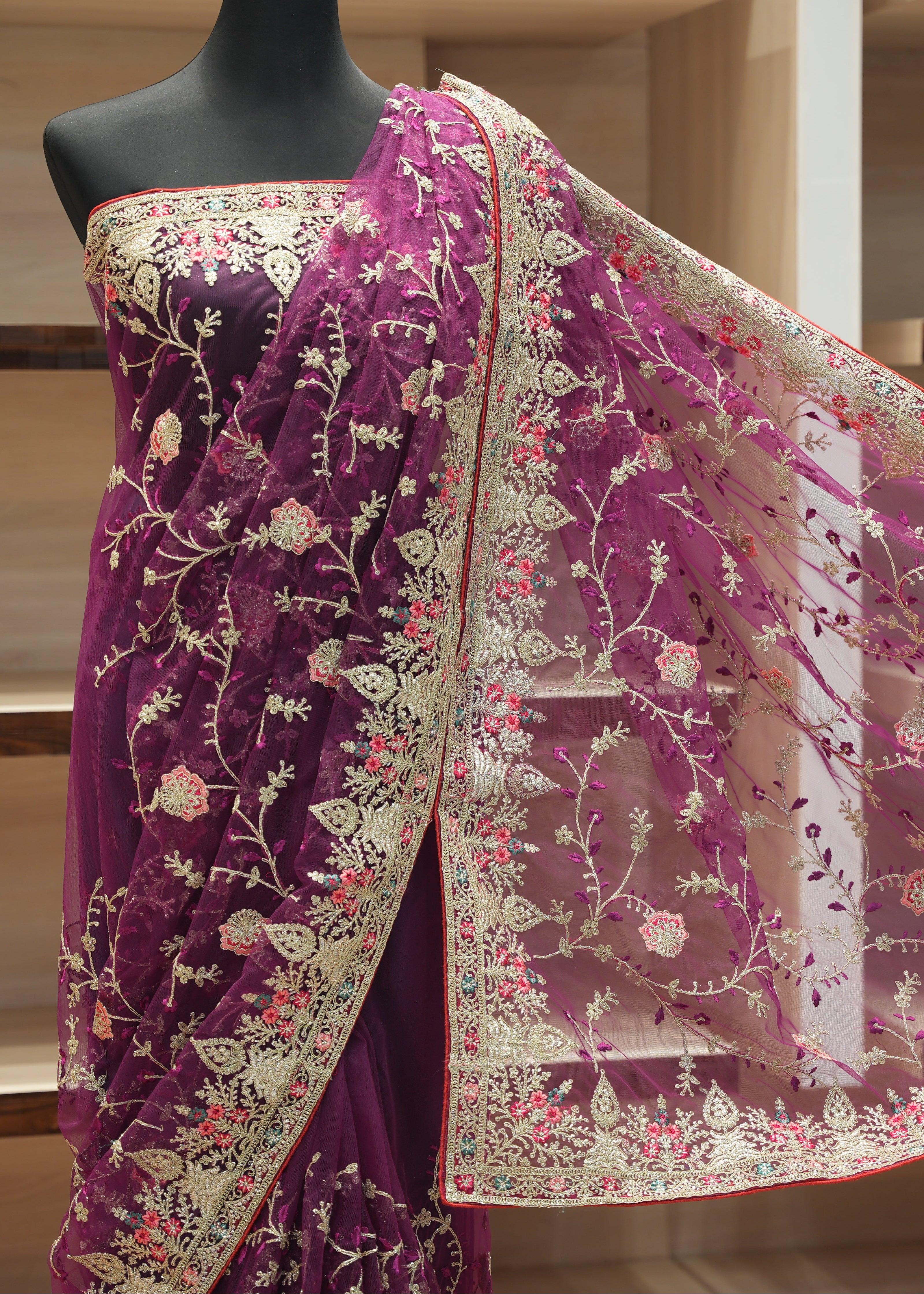 A deep purple georgette saree with intricate beige floral embroidery and a red border, draped on a black mannequin torso. The matching sheer net dupatta is spread out to the right, showcasing the detailed embroidery and border design.