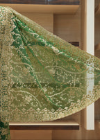A green embroidered fabric drape with ornate gold floral lace trim, displayed on a mannequin torso in front of wooden shelving.